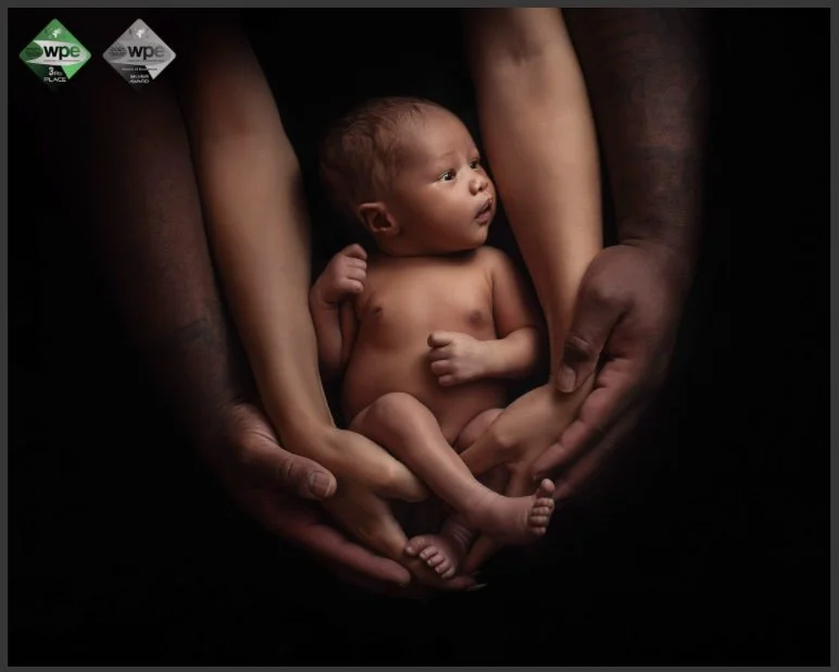 A newborn baby held gently by adult hands, with dark background.