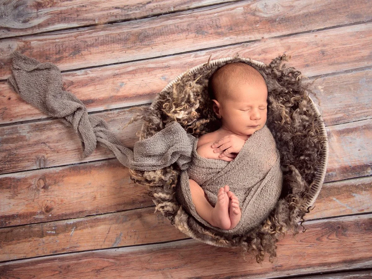Black and white photo of a tiny baby sleeping in a person's hands, with the person's arms and hands gently cradling the baby.