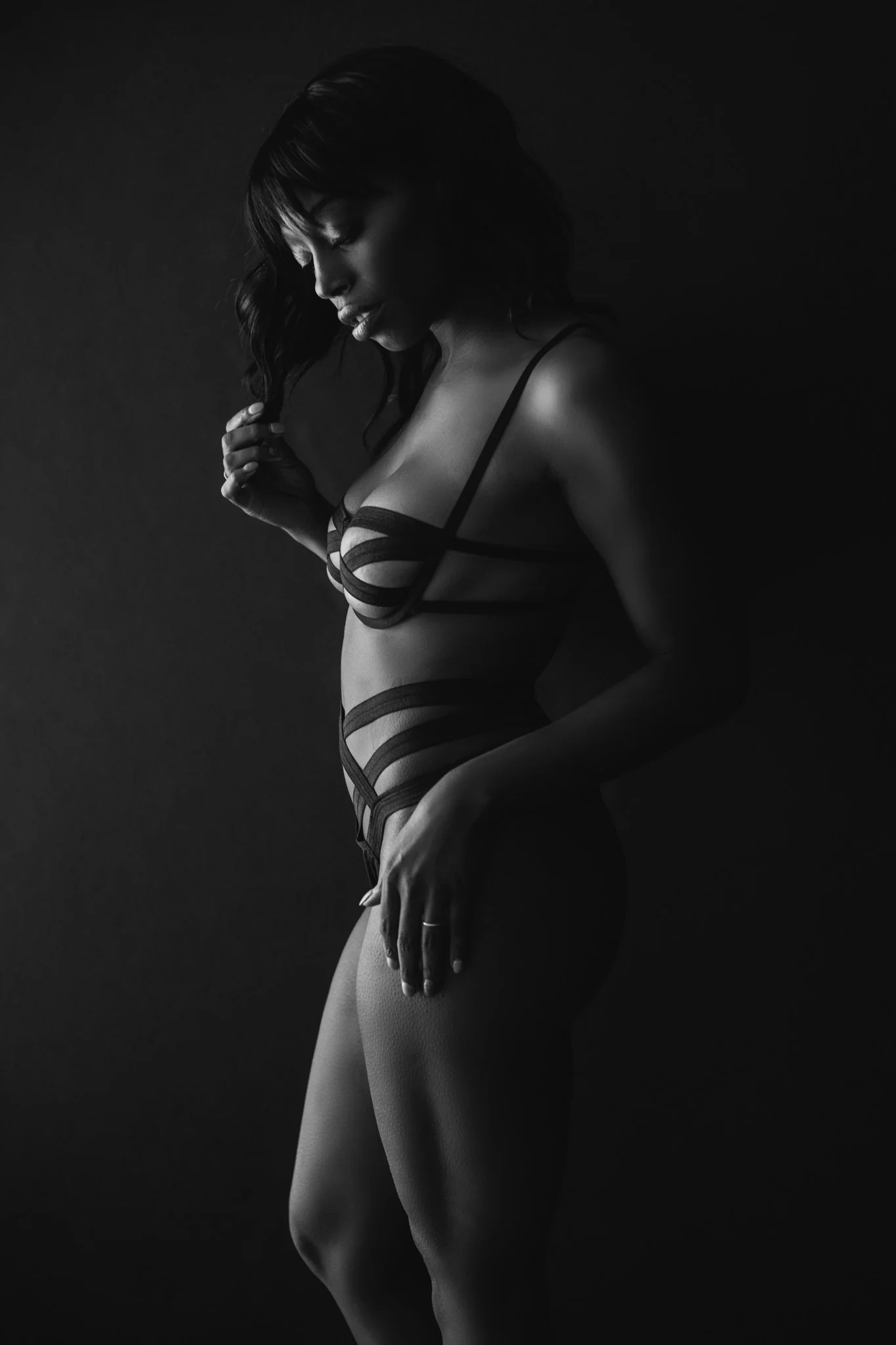 Black and white portrait of a woman in lingerie, posing against a dark background.