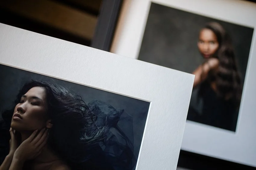 Two matted photo prints of women hanging on a wall, one in the foreground and one slightly blurred in the background.