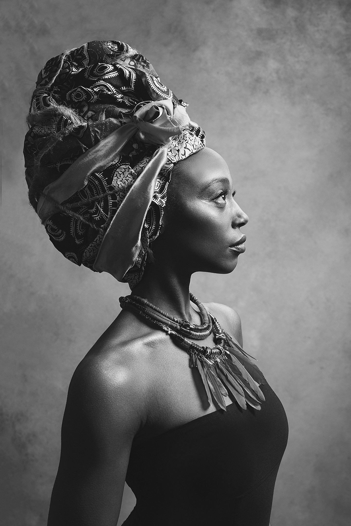 An elegant black and white portrait of an African woman wearing a headwrap, layered necklaces, and a strapless top.