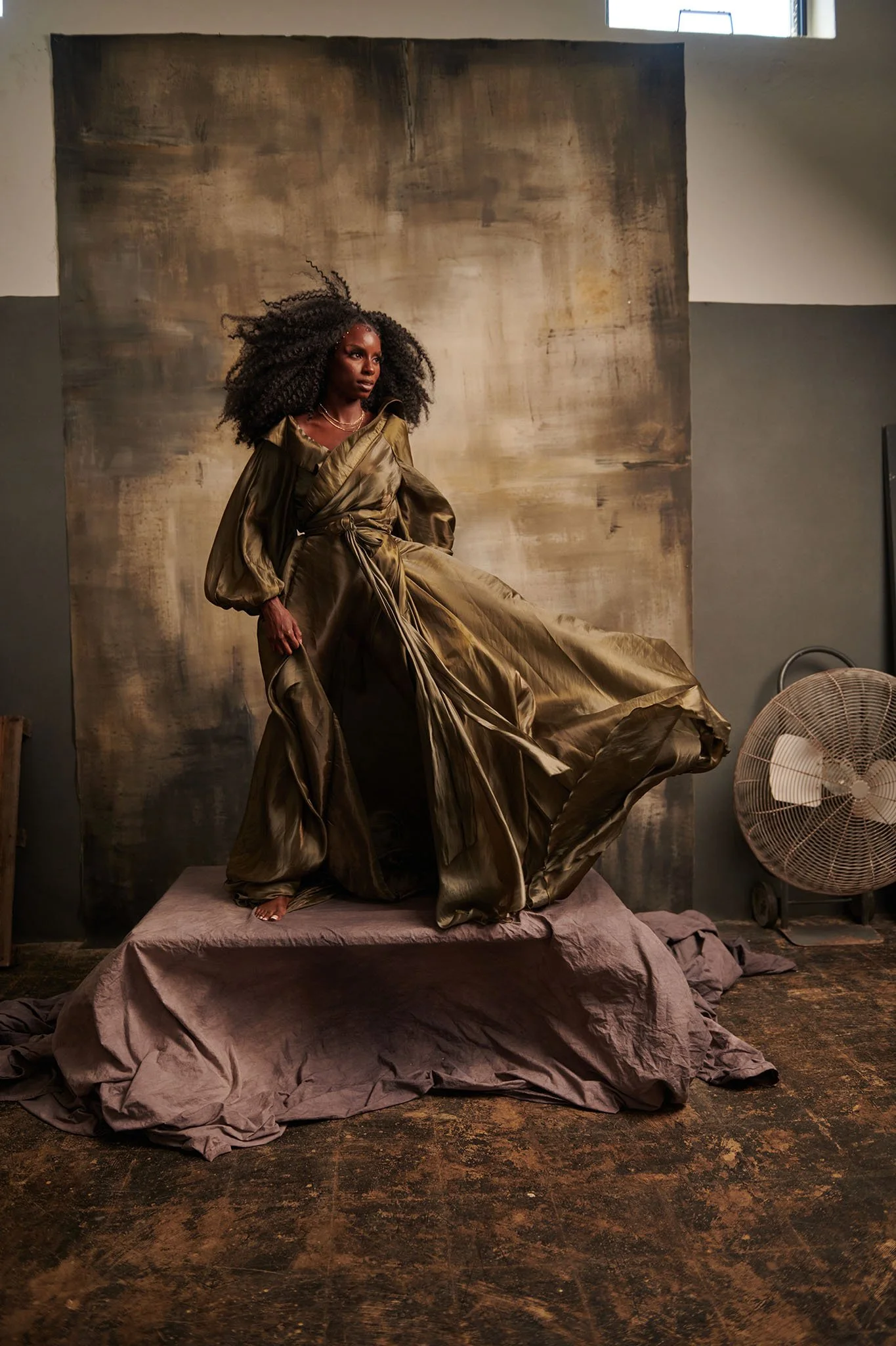 A woman in an elegant, metallic gold gown standing on a platform in a studio setting.