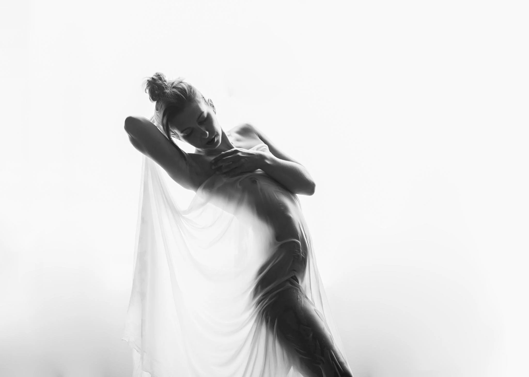 A woman in a flowing dress poses with one arm raised and her head tilted, against a plain background.