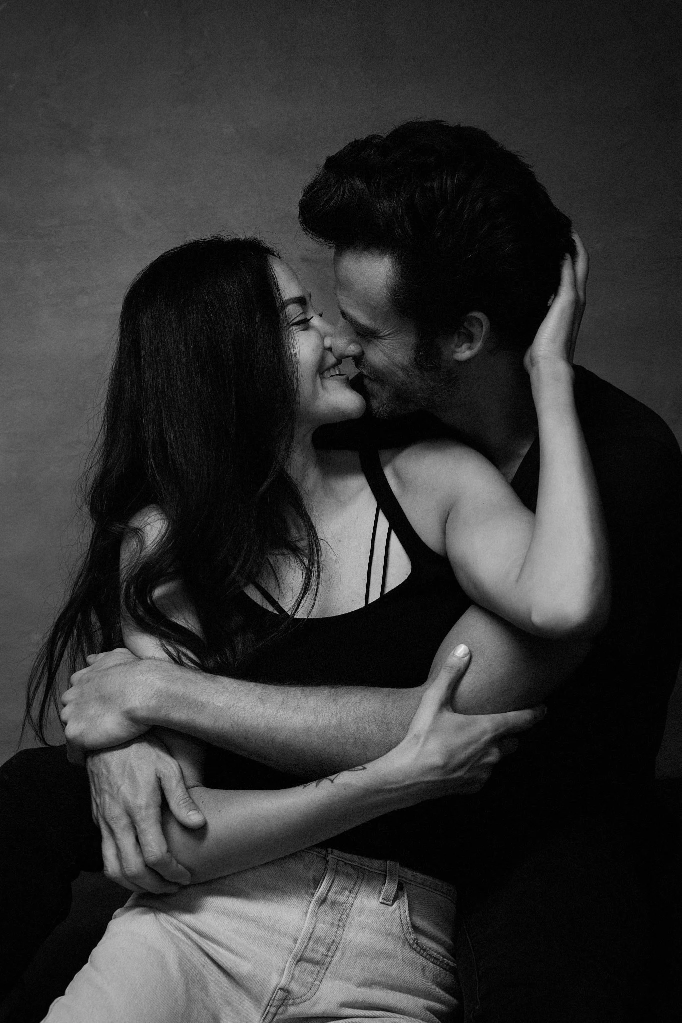 A black and white photo of a couple embracing and touching foreheads, smiling and showing affection.