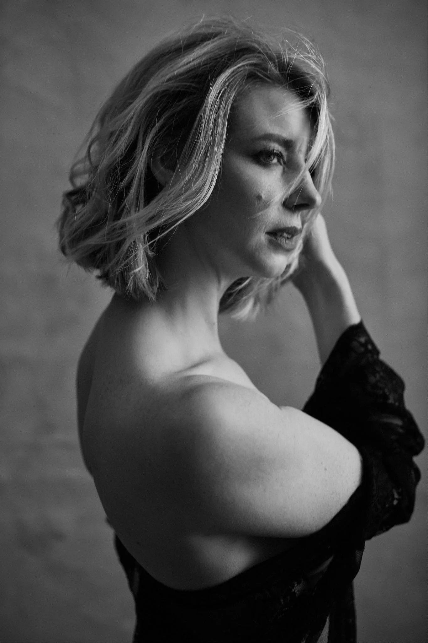 Black and white portrait of a woman with short, wavy hair, looking to the side, wearing lace gloves.