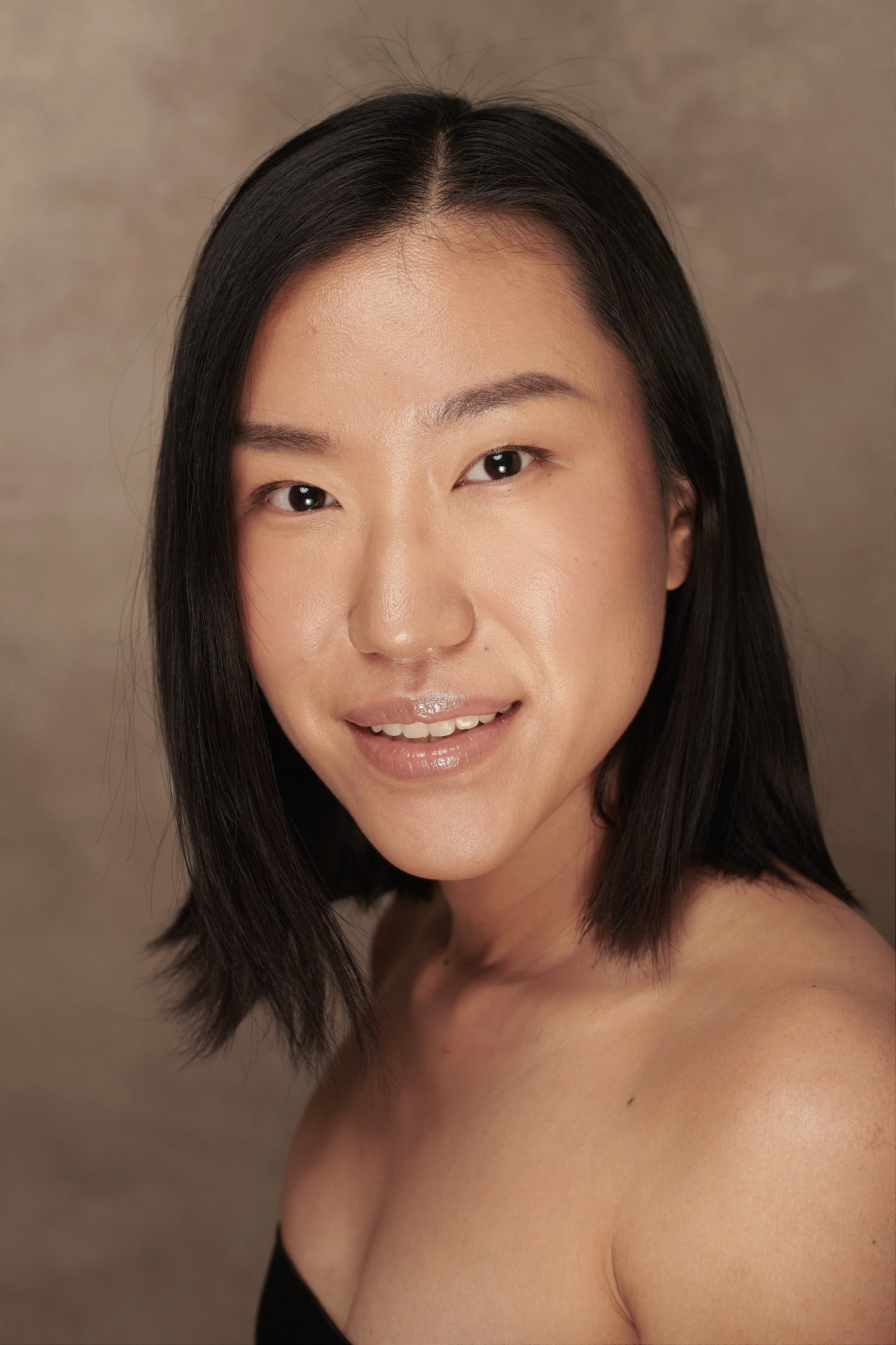 Portrait of a woman with shoulder-length black hair, smiling, set against a neutral background.