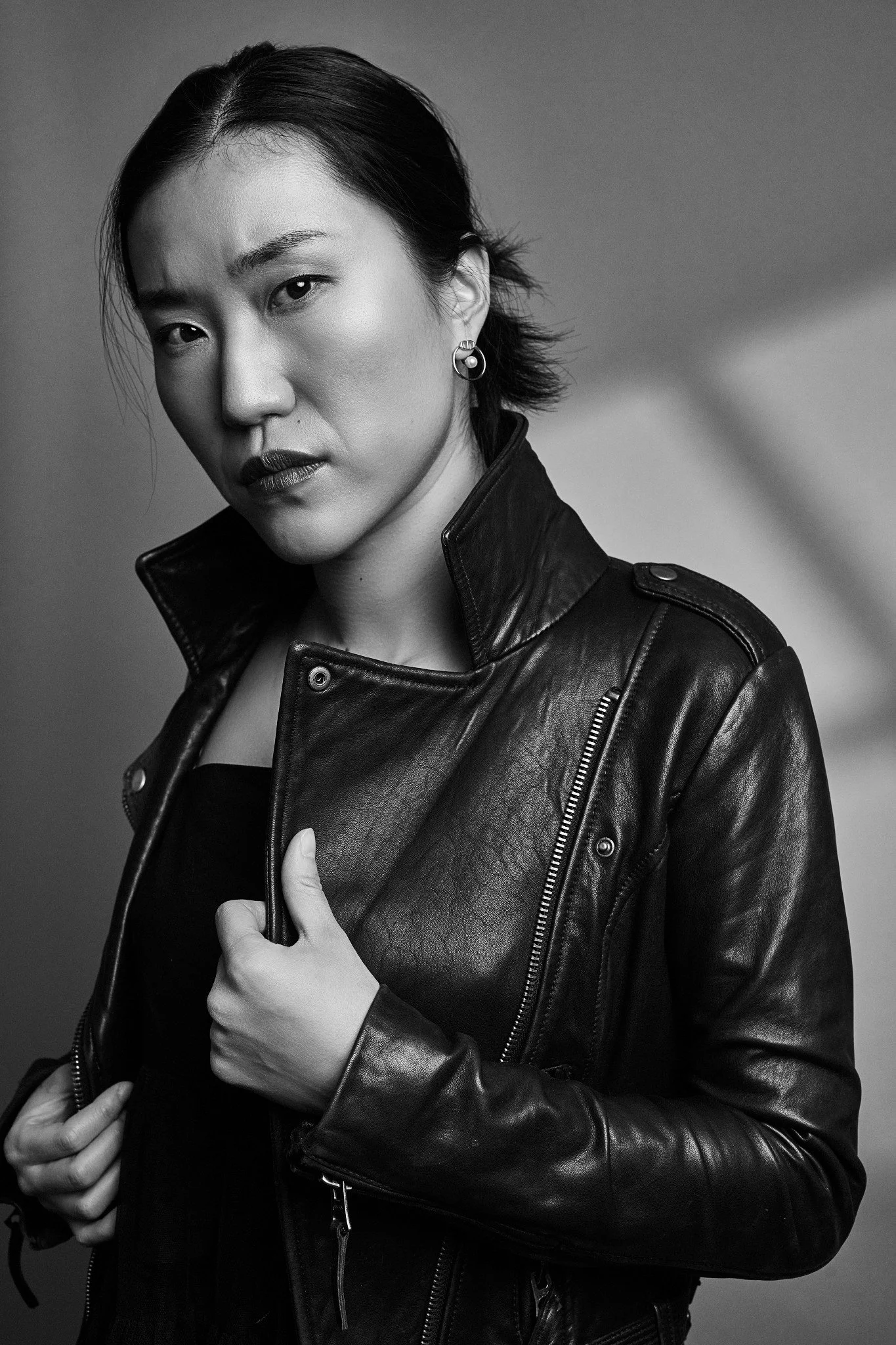 Black-and-white portrait of a woman with short dark hair, wearing a leather jacket, looking serious, and slightly tilting her head.
