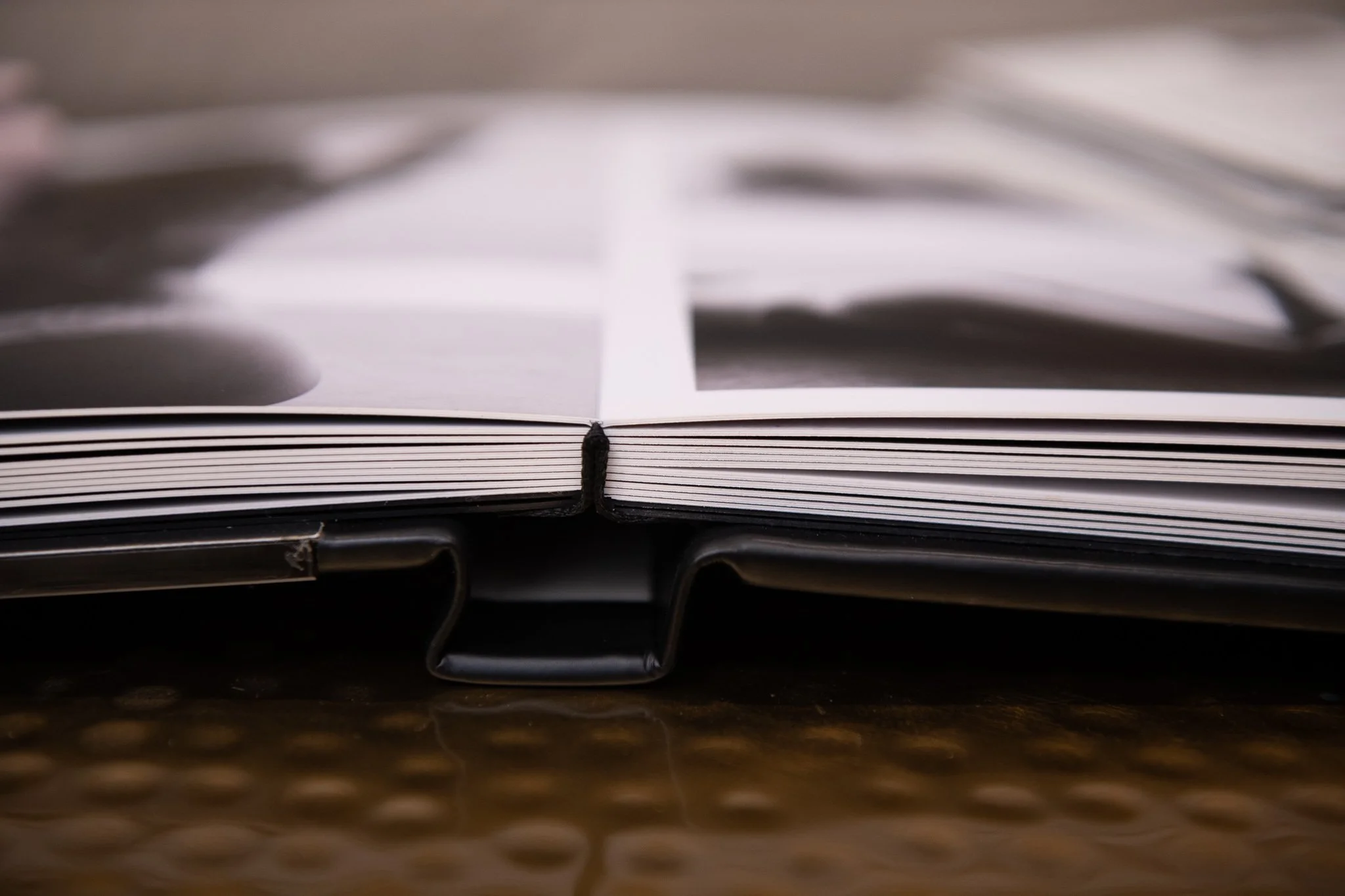 Close-up of an open photo album with black binding, lying on a textured surface, pages slightly curved and blurred images inside.