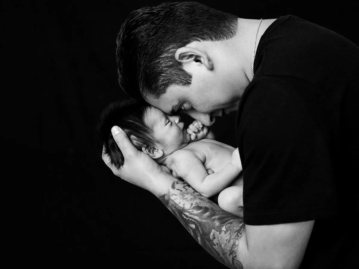 Black and white photo of a young girl lying on her back, wearing a knit hat, with her eyes closed and a calm expression. She is holding her chest with one hand and has a doll near her head.