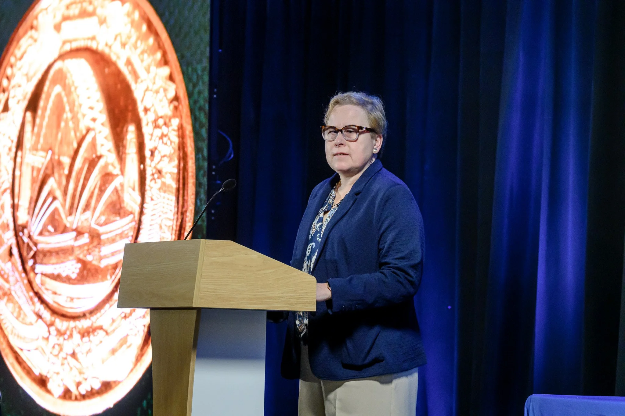 Carrie delivering a keynote at AARFP 2026 with Gold medal slide in the background 