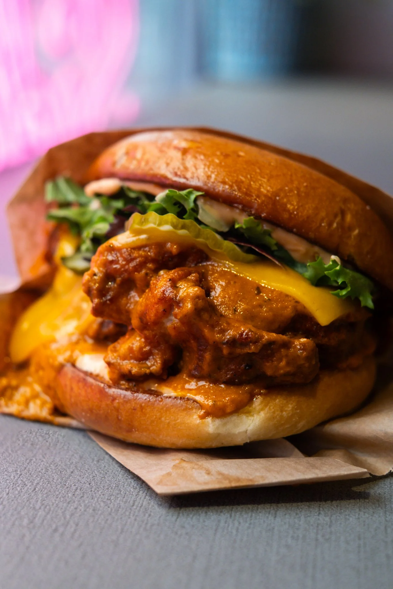 Close-up of a cheeseburger with lettuce, pickles, and sauce on a bun, with melted cheese and seasoned chicken patty.
