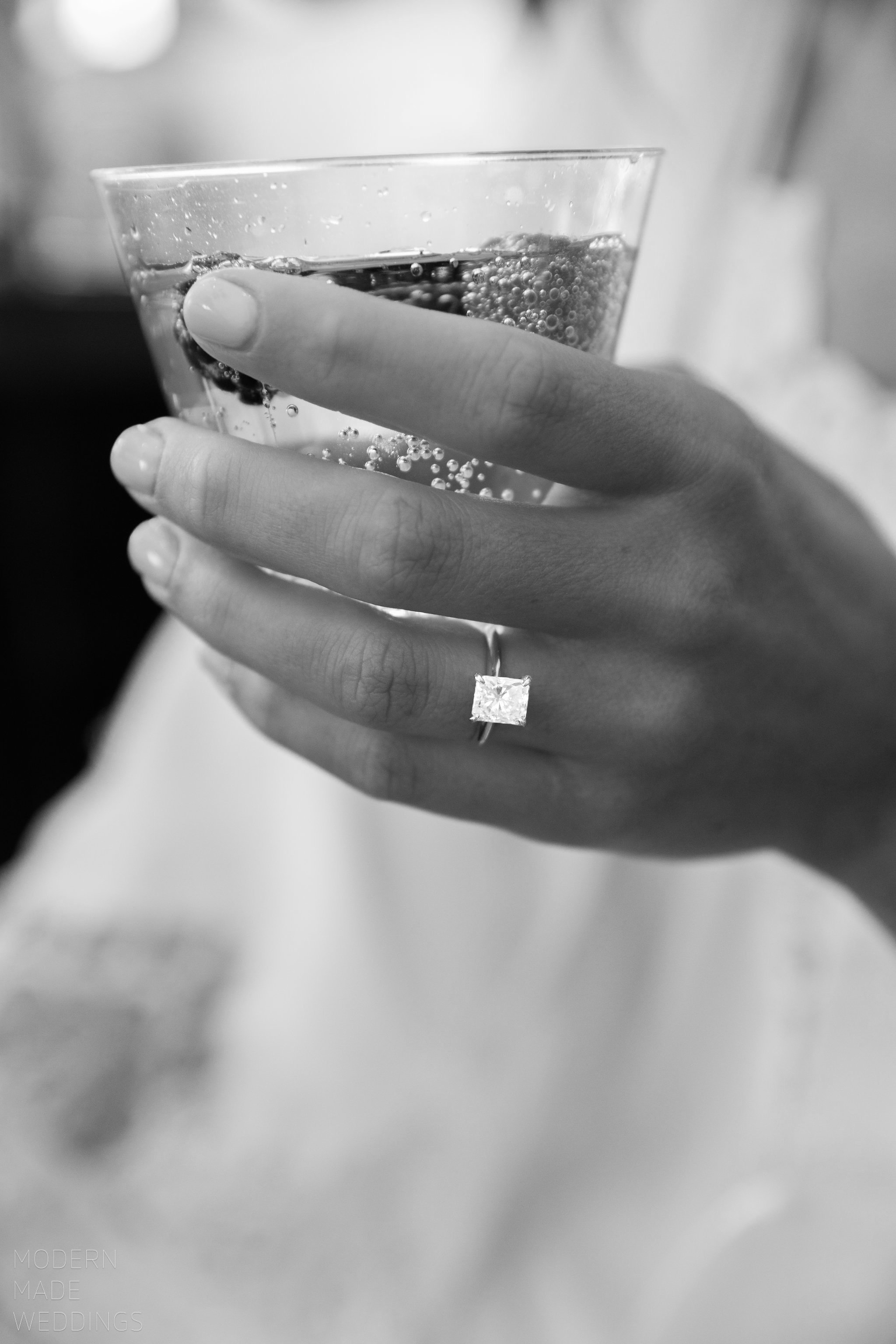 Close-up of a person's hand holding a glass of carbonated beverage with bubbles, with a focus on the hand, with a blurry background.