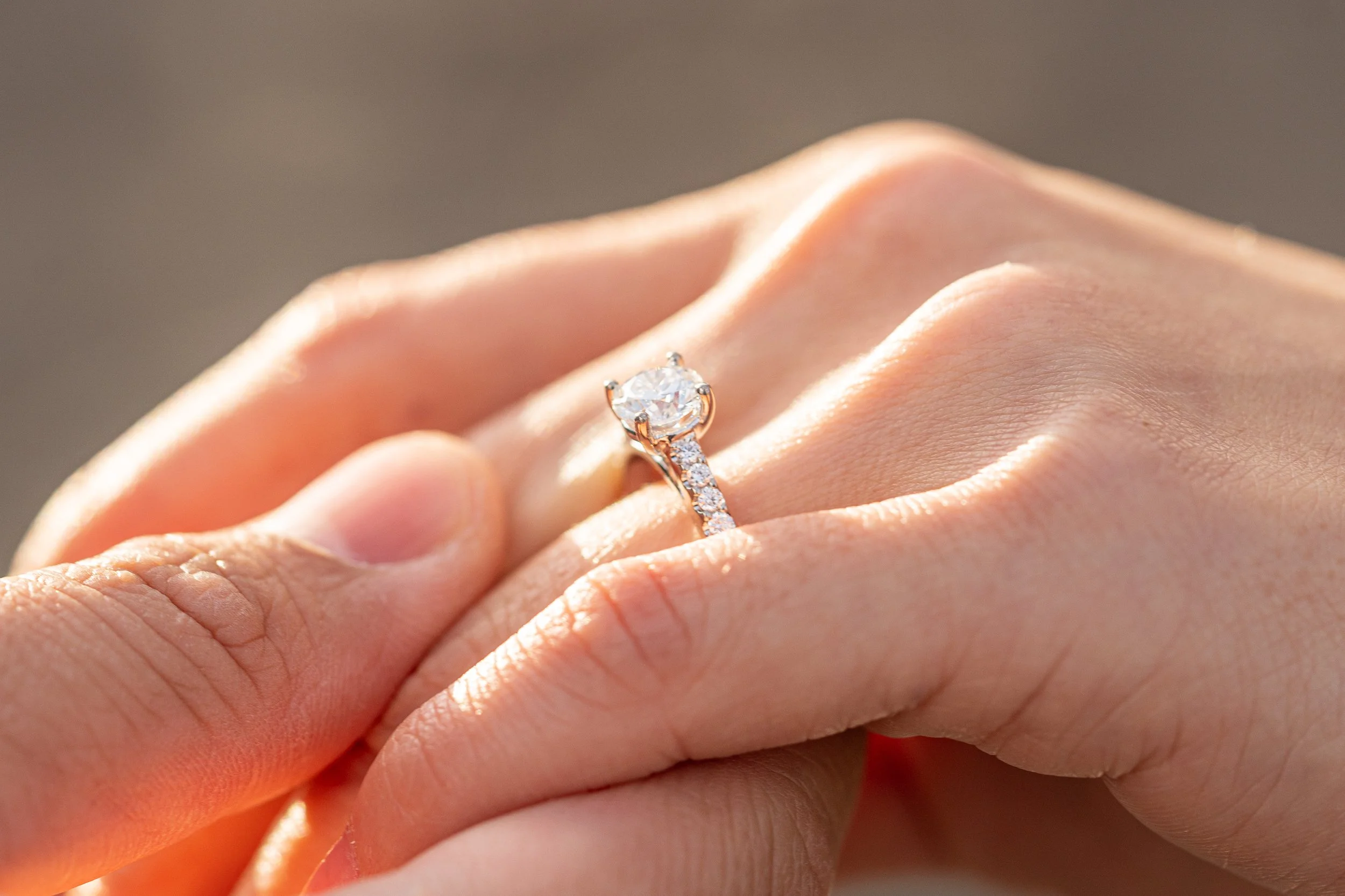 Close-up of a hand with an engagement ring featuring a large round diamond and smaller side diamonds.