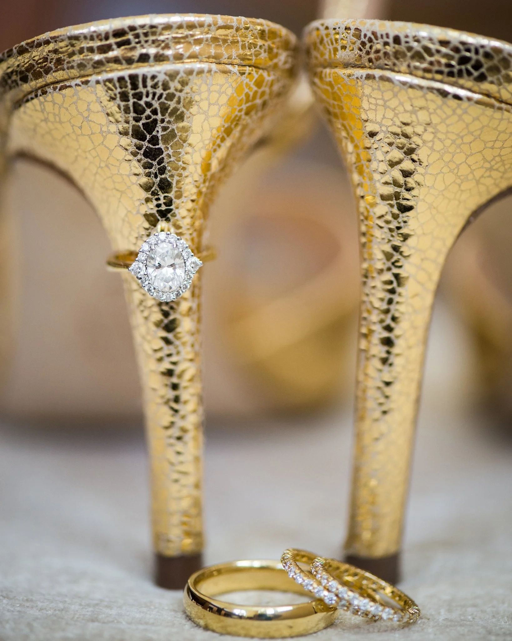 Close-up image of gold jewelry including two rings and two bangles, with one ring featuring a large central diamond surrounded by smaller diamonds, and the bangles having a textured pattern.
