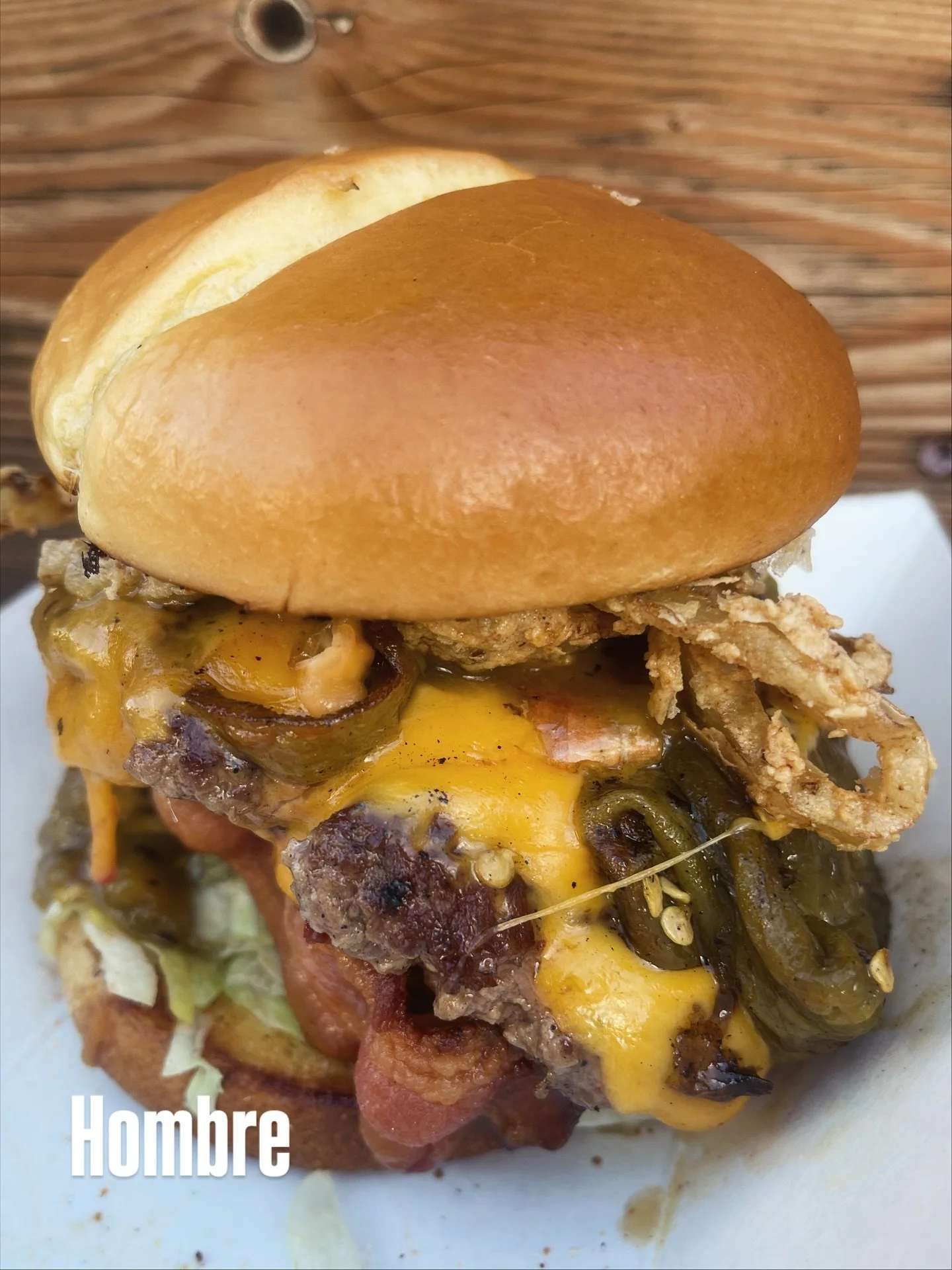 Hungry for The Hombre? 🔥 Green chile, aged cheddar, hickory-smoked bacon, and fried onion straws stacked on a signature @uglyponysaloon Angus smash patty — all on a toasted brioche bun. Our guest was very satisfied with his choice after debati