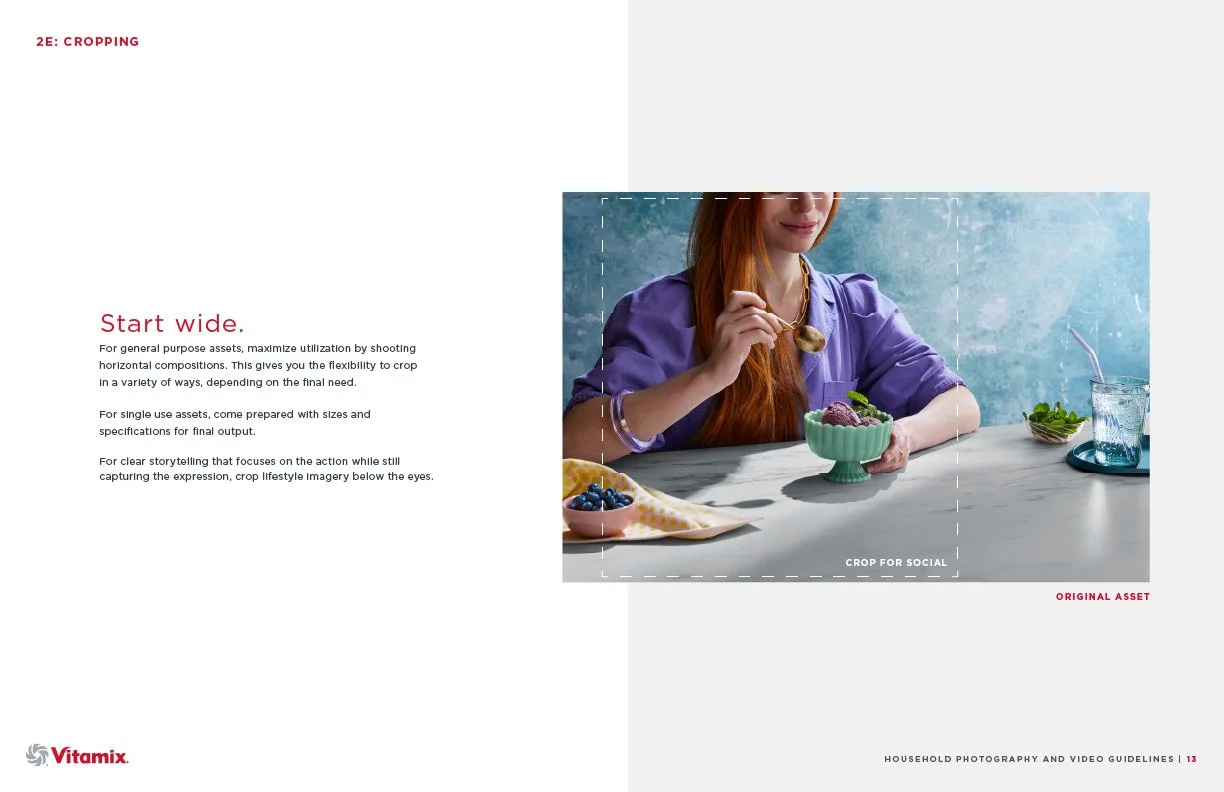 A woman with long red hair wearing a purple top is sitting at a table, eating a bowl of purple and green ice cream or yogurt, with greenery and blueberries on the table, and a glass of water with a straw in the background.