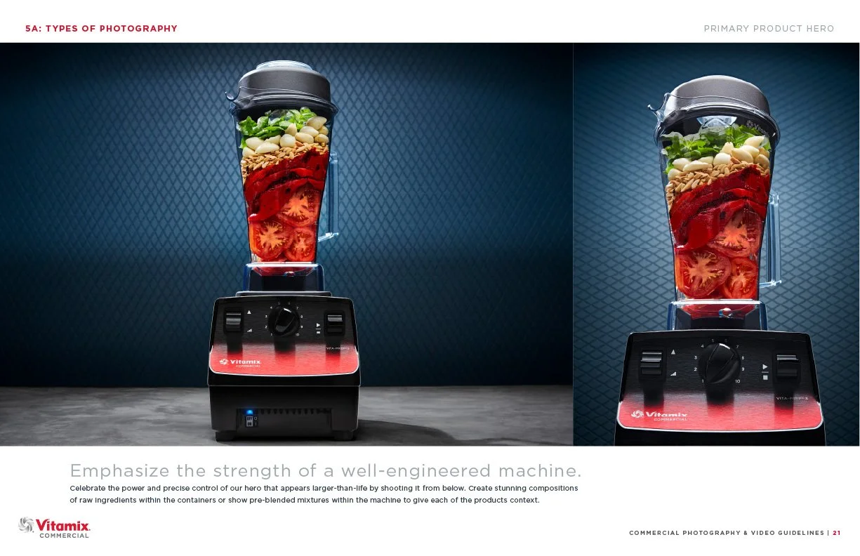 A blender filled with layers of chopped tomatoes, garlic cloves, nuts, bread slices, and green herbs, set against a textured blue background.