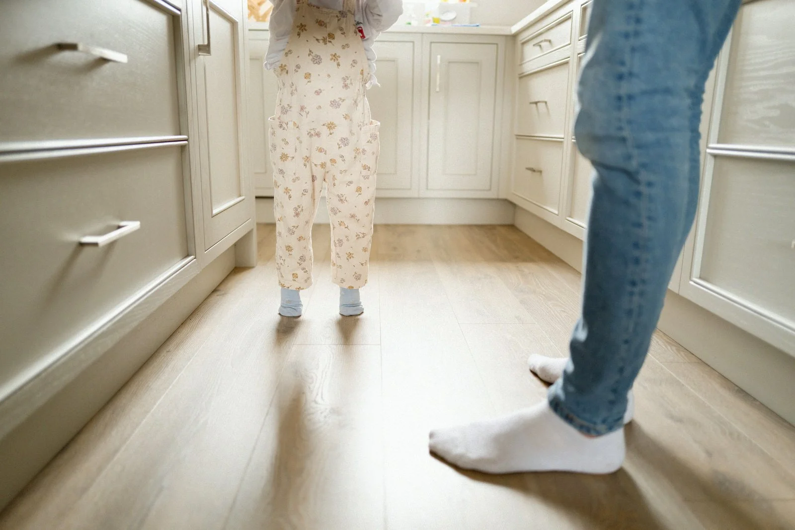 Close-up of two people standing in a kitchen, wearing socks, with a child in pajamas facing away and an adult in jeans.