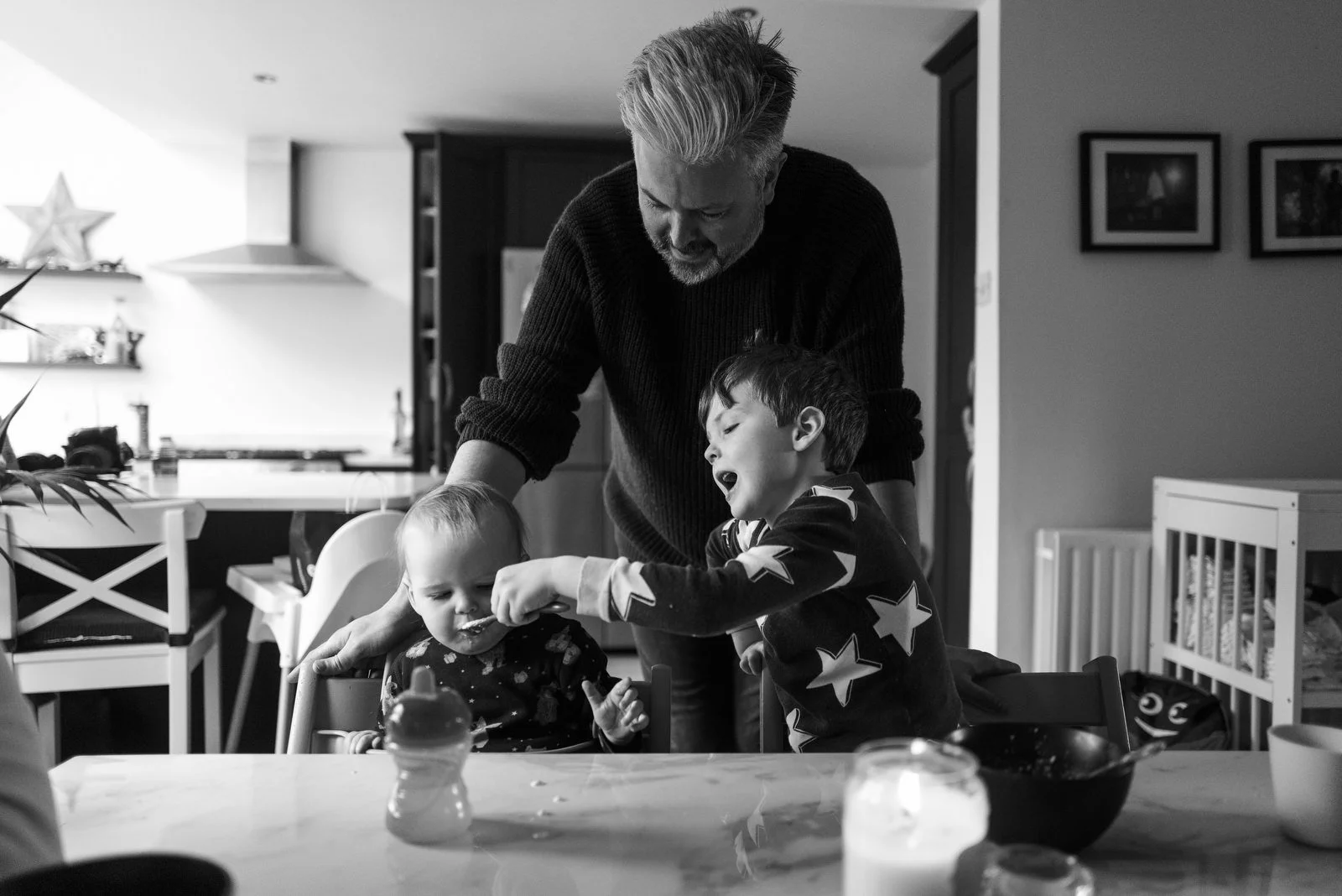 A man feeding two young children at a kitchen table.