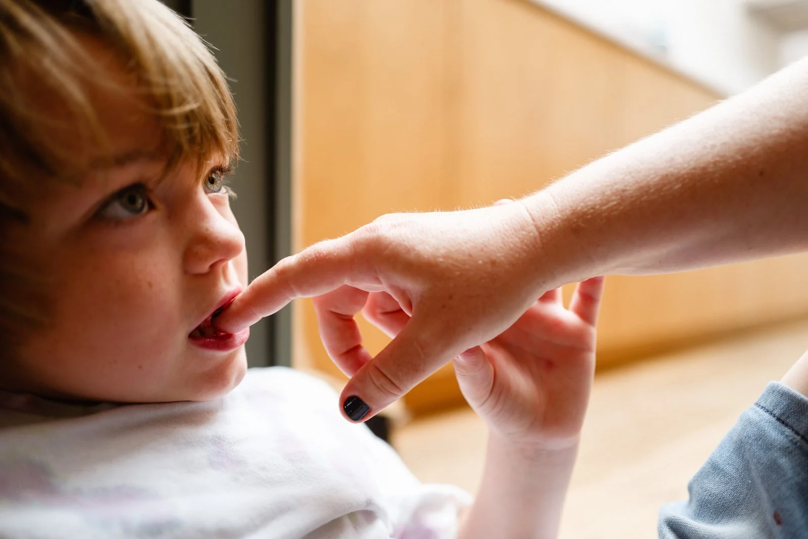 A young boy with light-colored hair and freckles looks up as an adult's hand touches his nose.