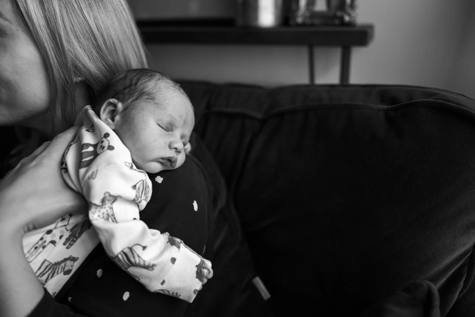 A baby sleeping on a person's chest with an adult holding the baby, with part of the adult's face and shoulder visible, and the scene is in black and white.