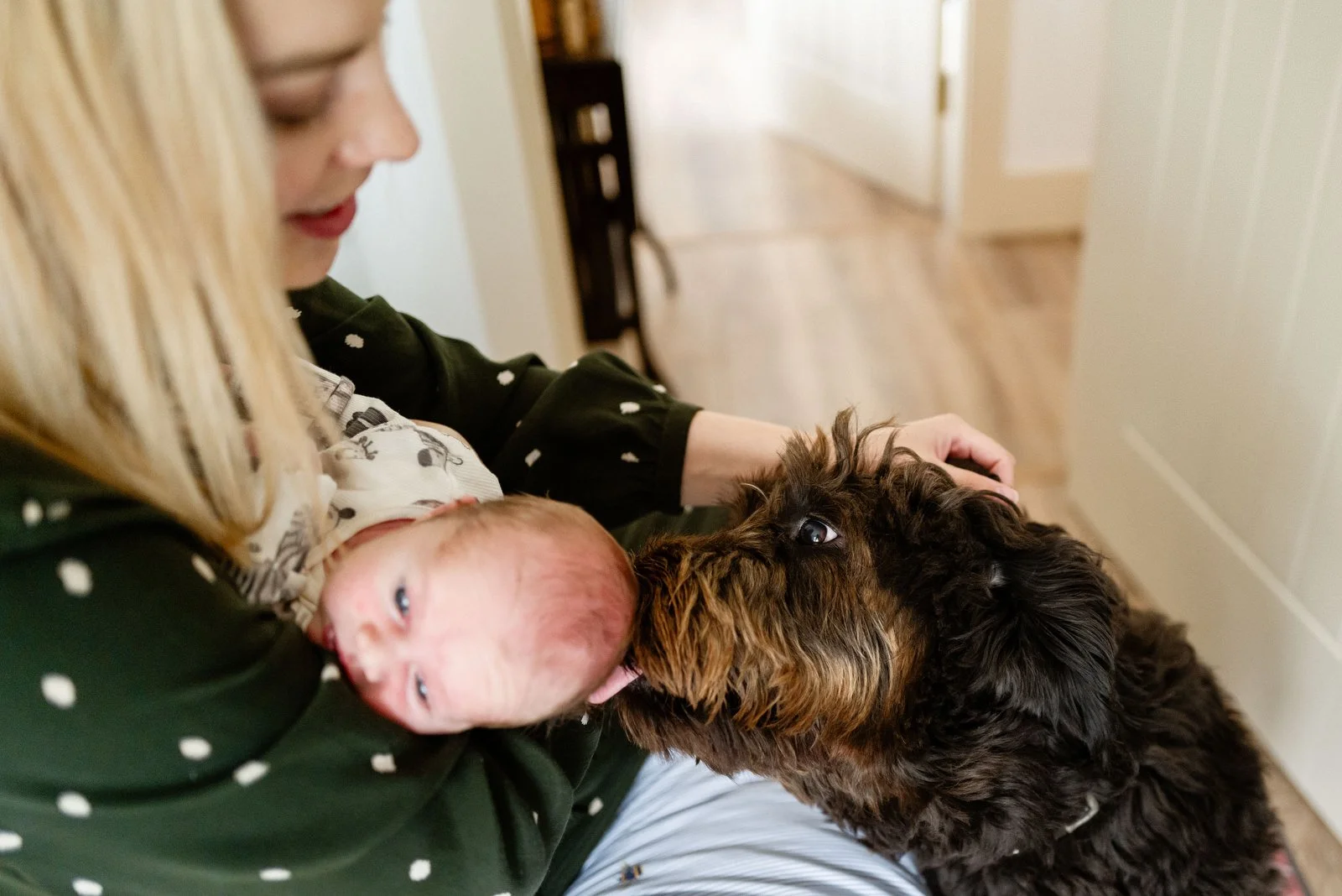 A woman holding a newborn baby and a puppy in an indoor setting.
