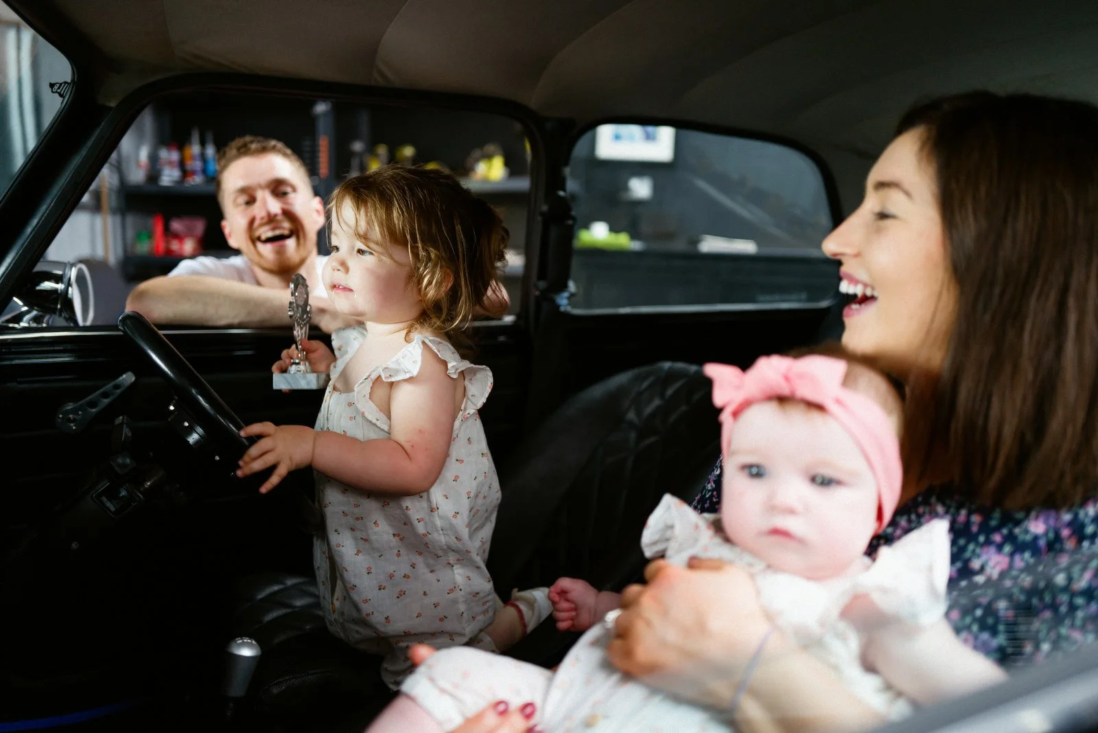 A family inside a vintage car with children and mother smiling and a father sitting inside the car.
