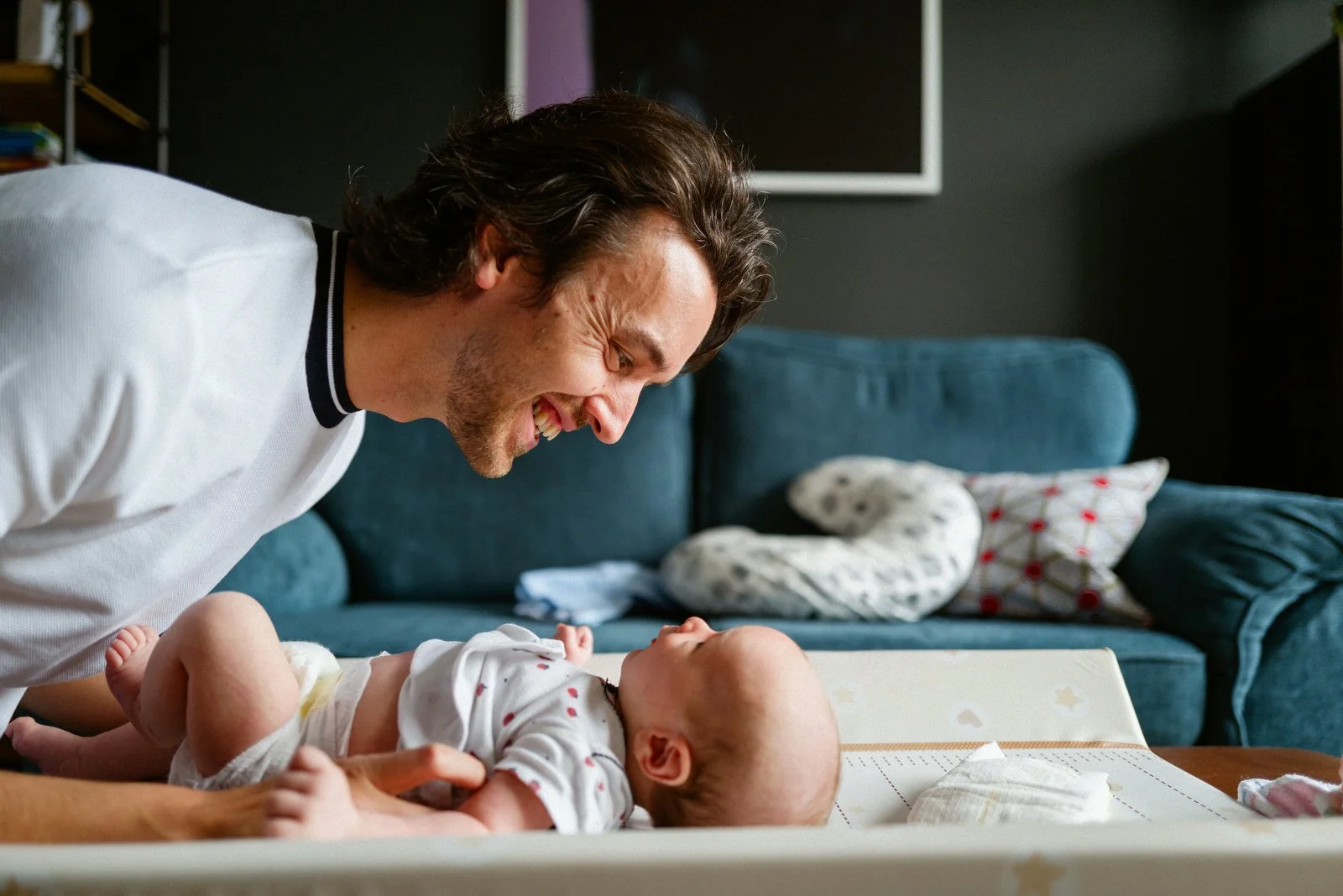 A man is smiling and leaning over a baby lying on a changing table indoors.