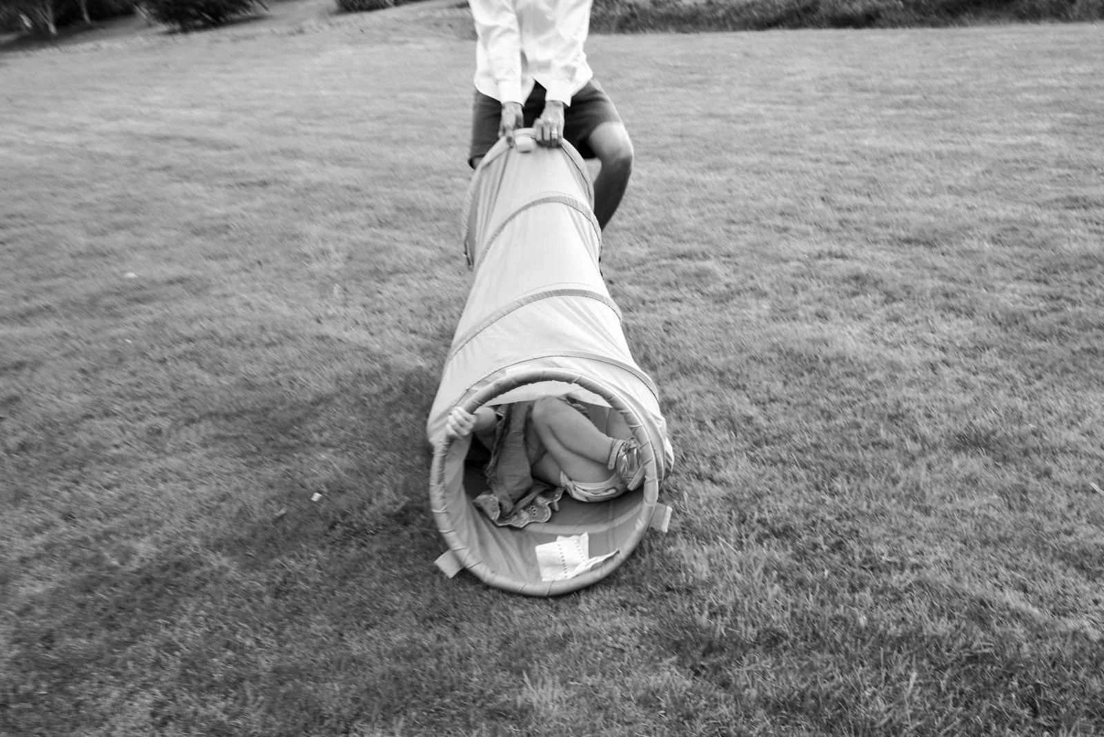 Child crawling on the grass with an adult pushing a tunnel toy