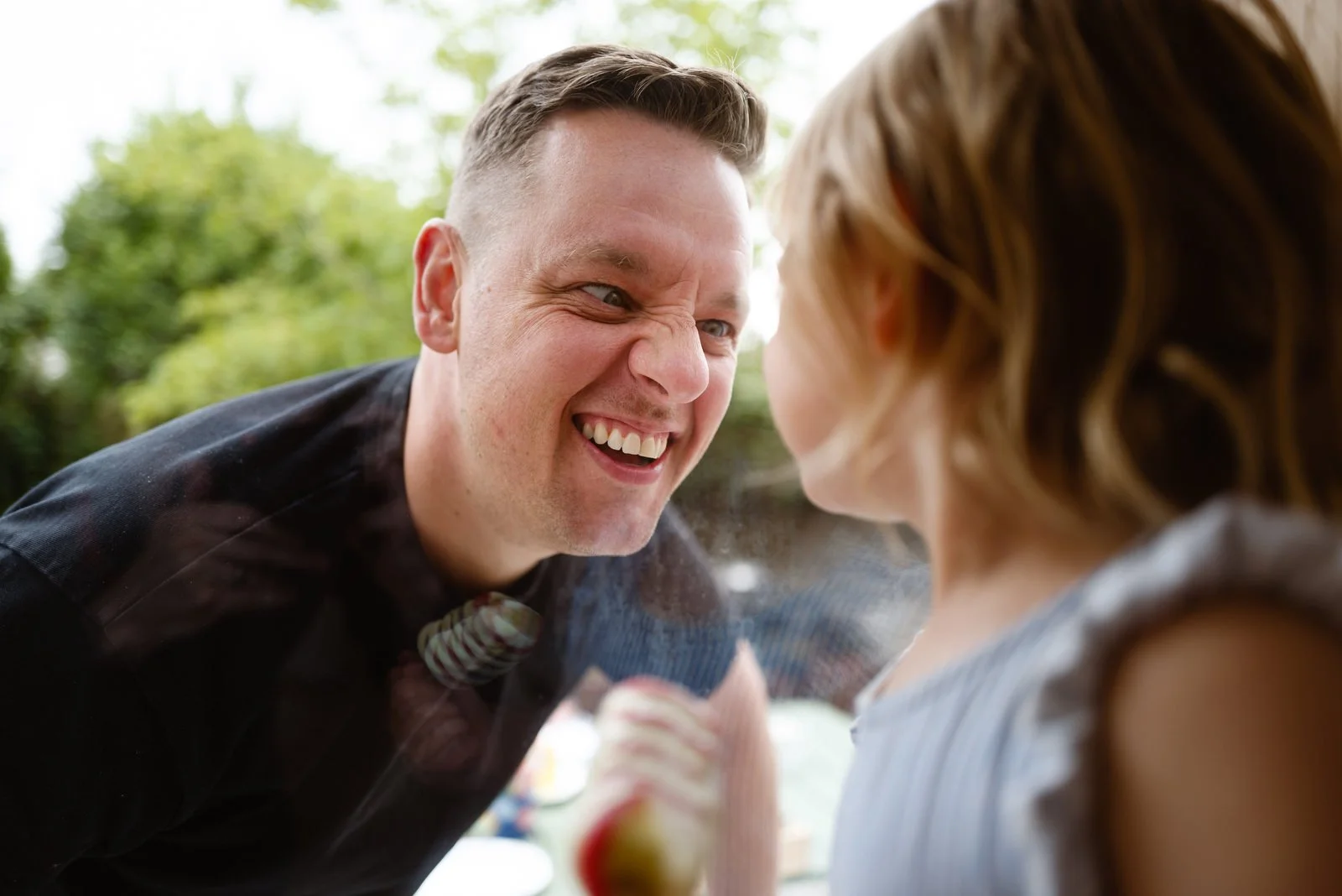 A man and a woman face each other smiling and laughing outdoors.
