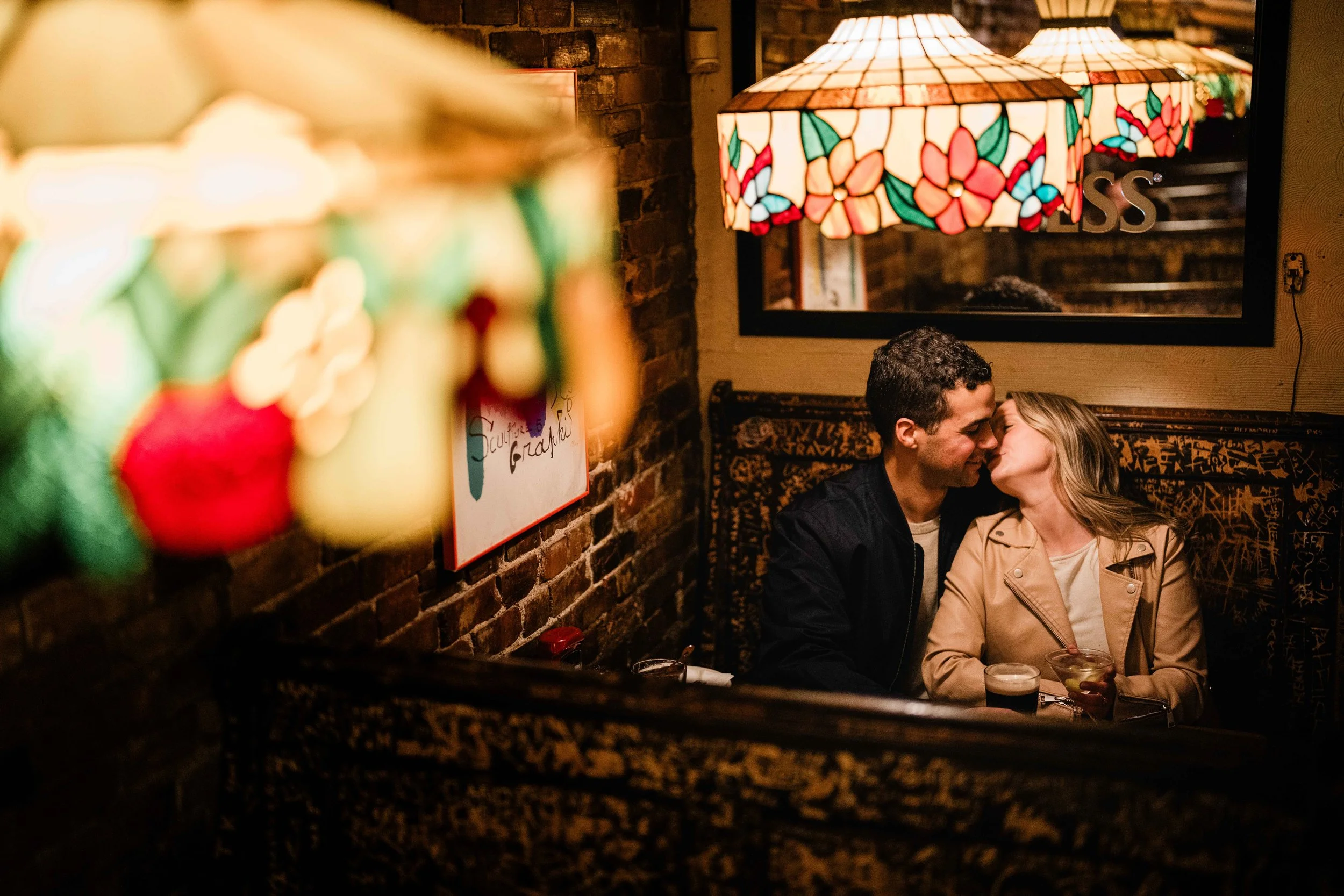 Couple kissing in a cozy dimly lit restaurant booth with colorful stained glass lamps.