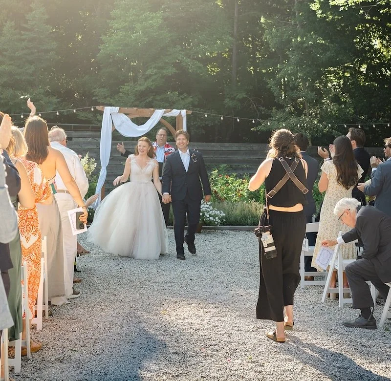 Julia Warner photographing bride and groom walking down the aisle at Caswell Farm