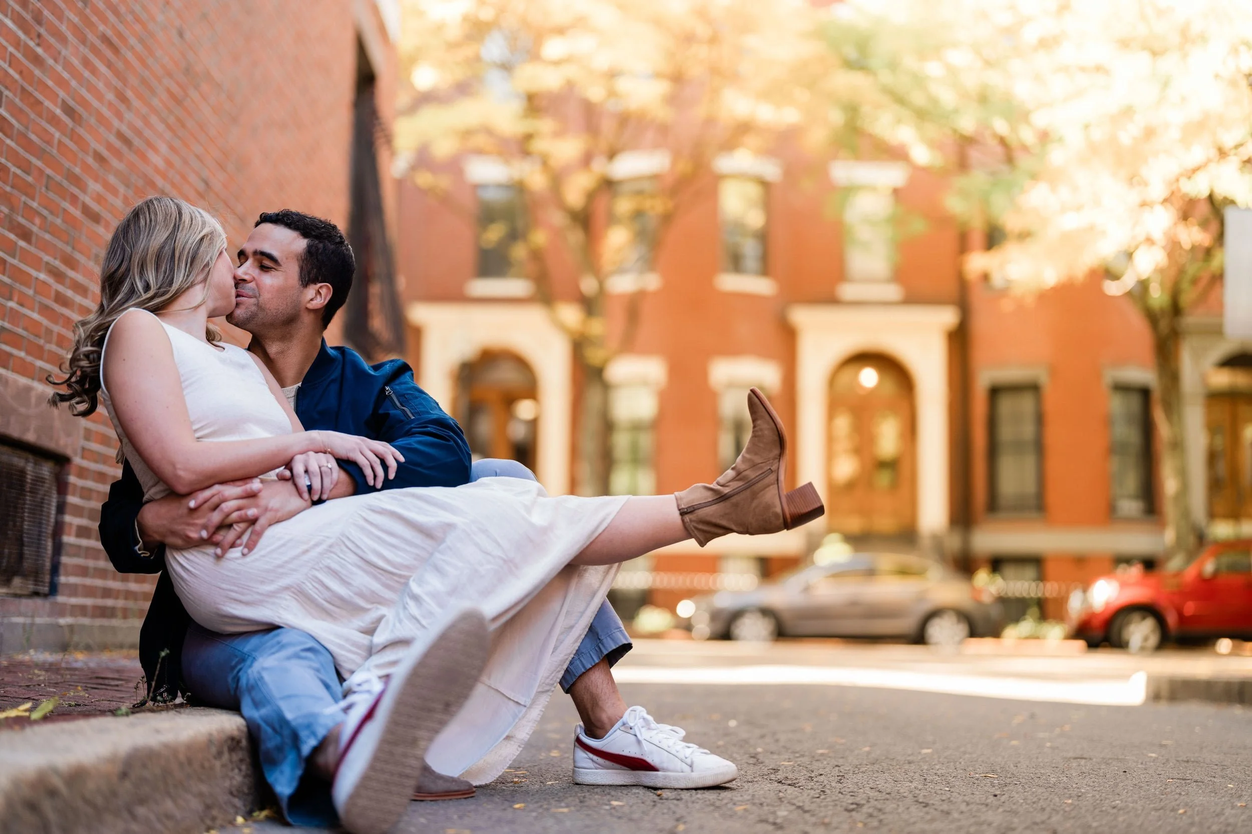Recently engaged couple sitting on the streets of downtown Boston kissing during an egagement photo session with Warner Photography