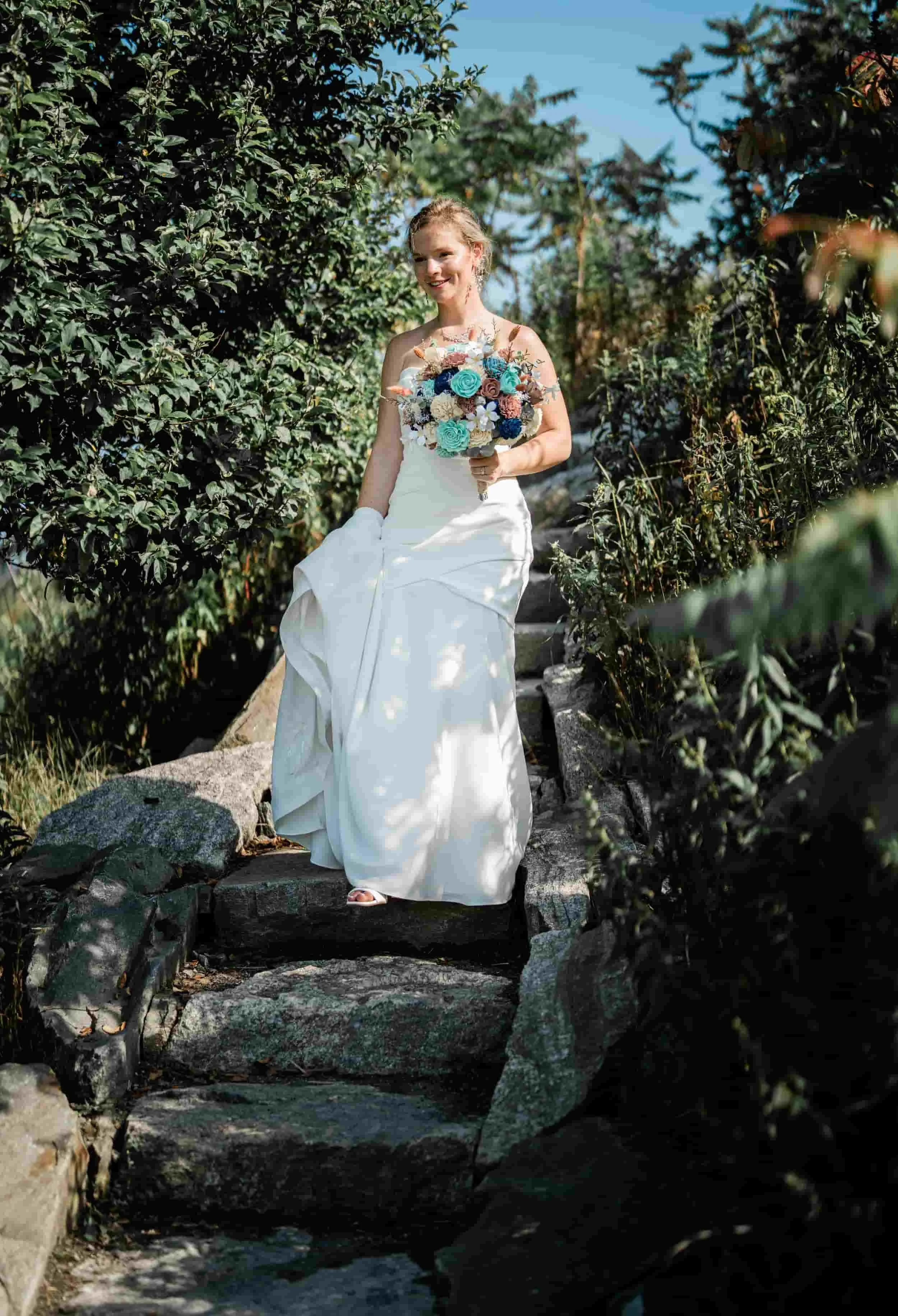 Bride standing on rocky shoreline with bouquet, Portland Head Light wedding portraits.