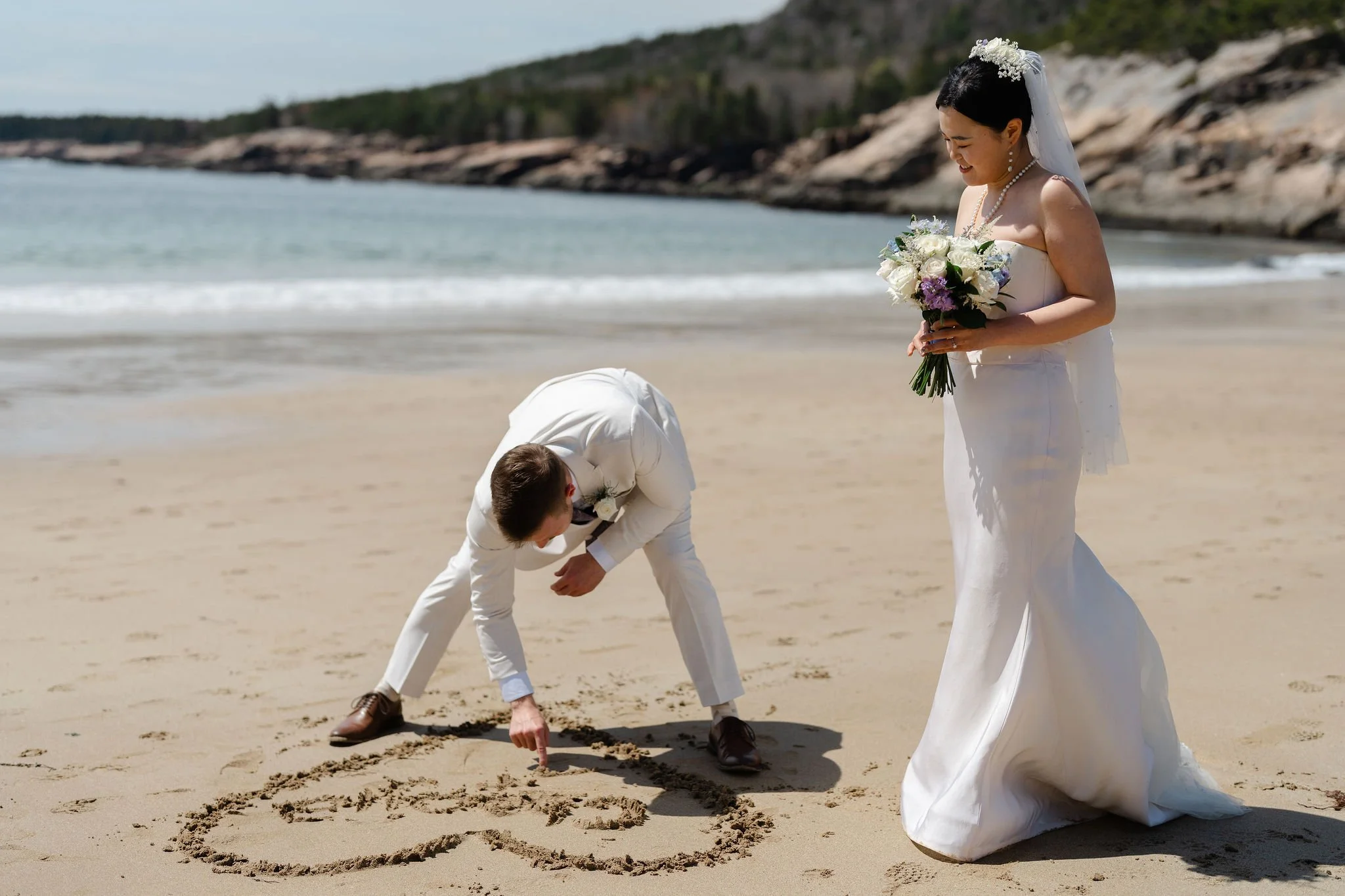 Groom drawing a heart in the sand during Acadia elopement on Sand Beach