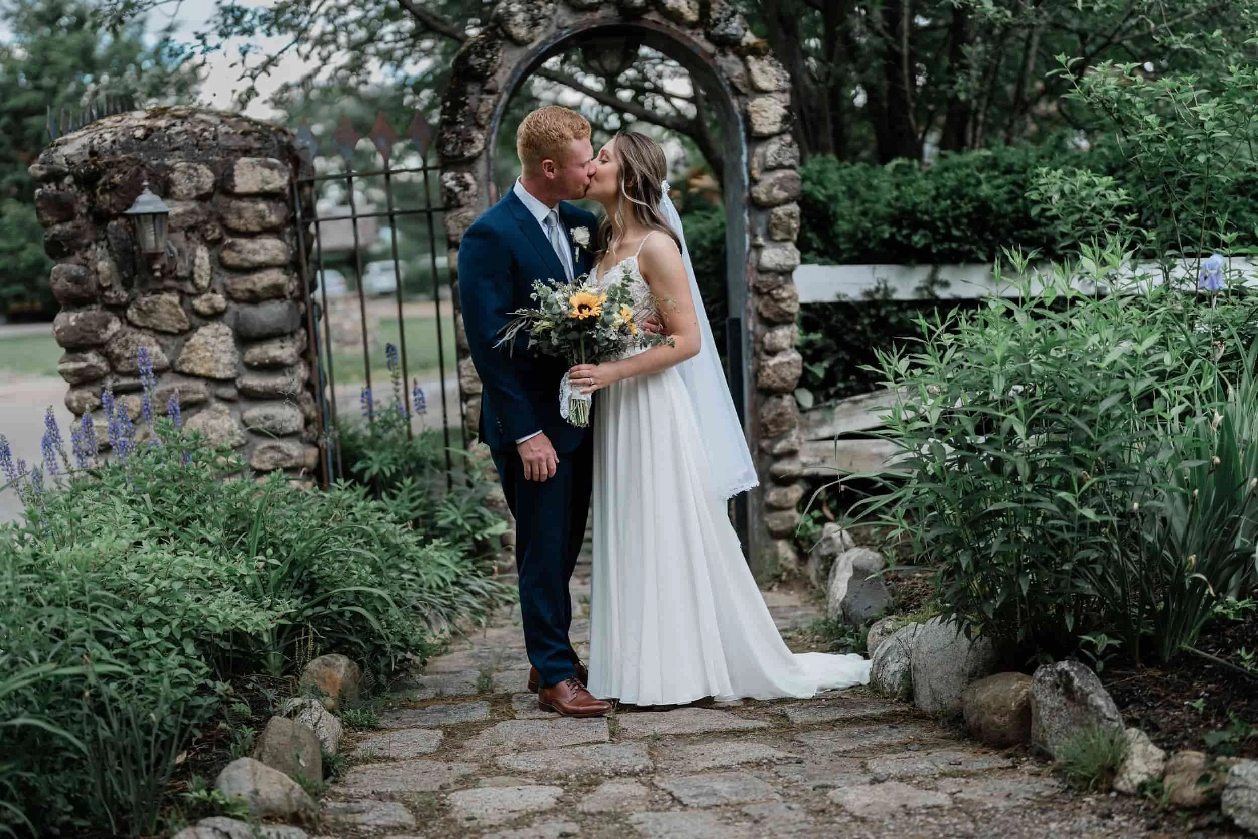Bride and groom kissing under stone archway at Old Saco Inn in Fryeburg, Maine.