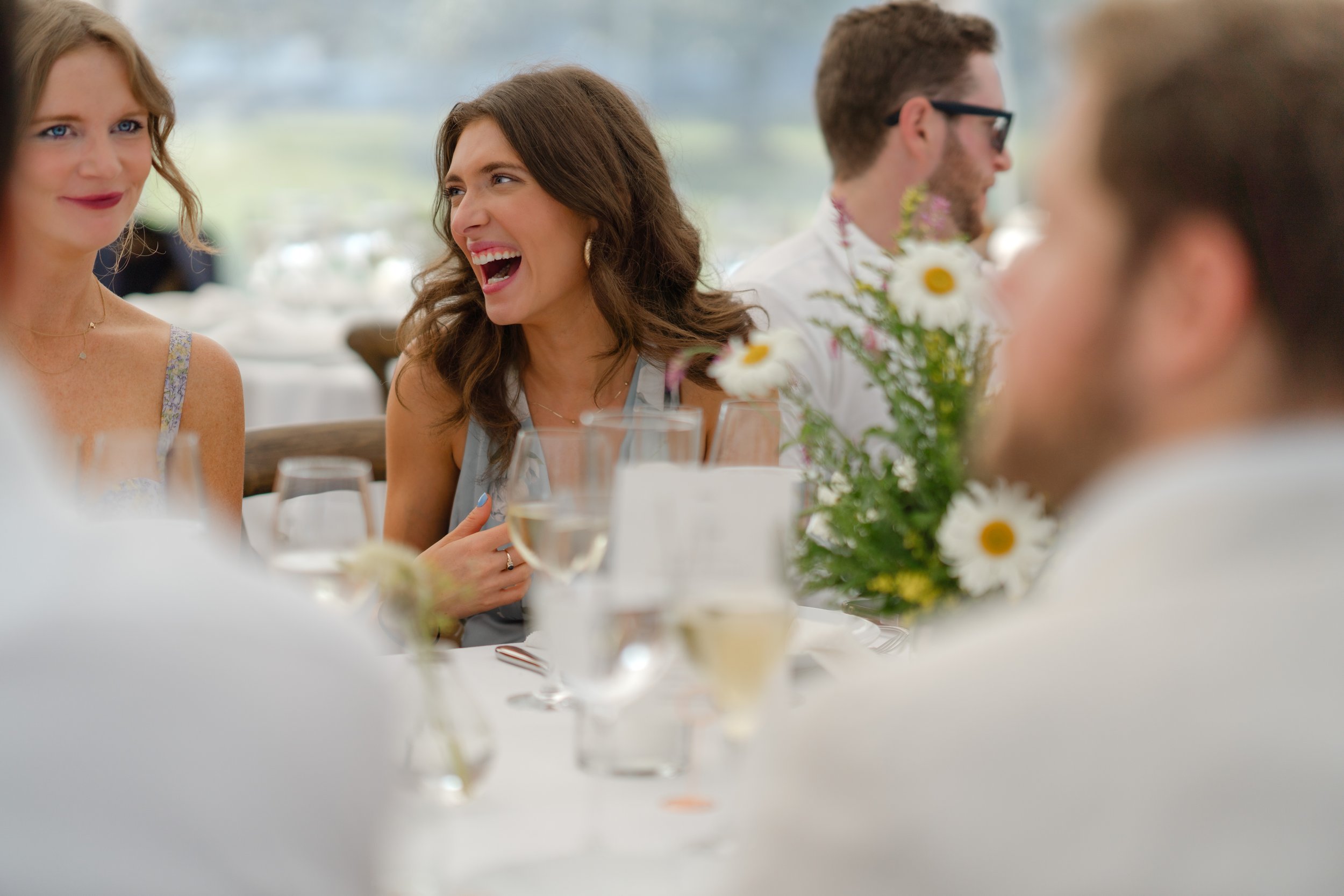 People laughing and talking at a table during a celebration, with flowers and drinks in front of them.