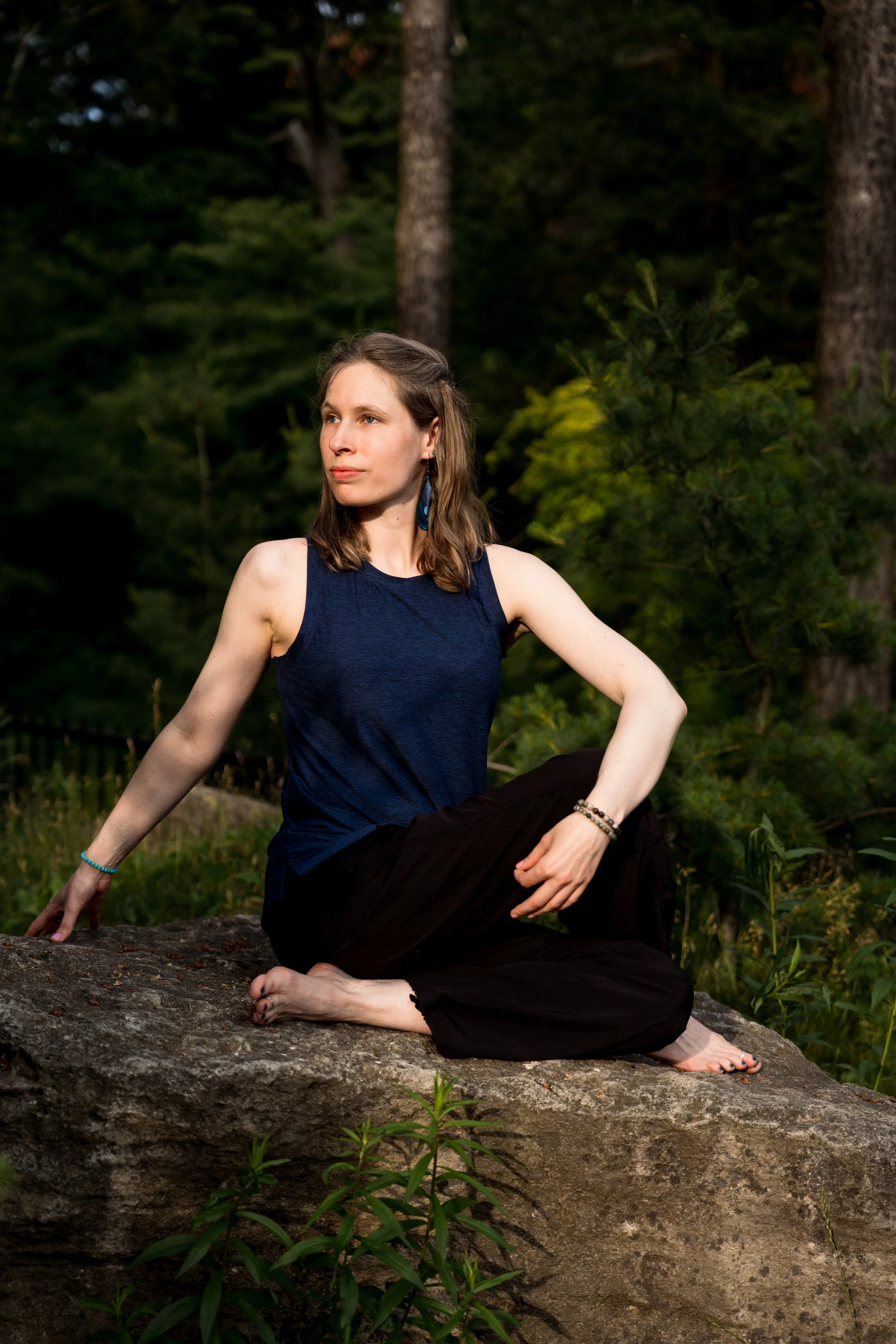 Anna peacefully in a seated twist on a rock in the forest.