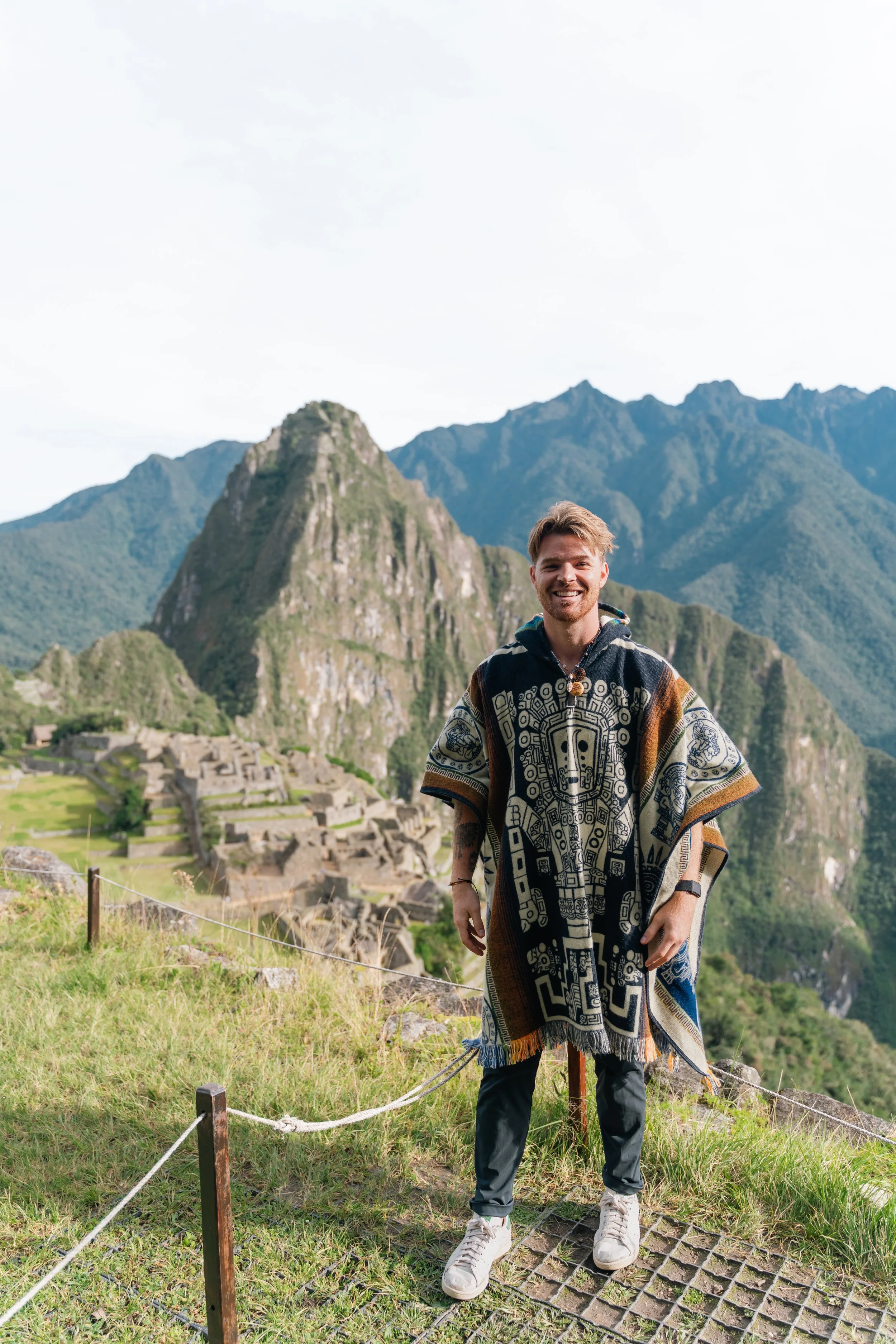 A smiling man standing outdoors with Machu Picchu and its mountainous landscape in the background.