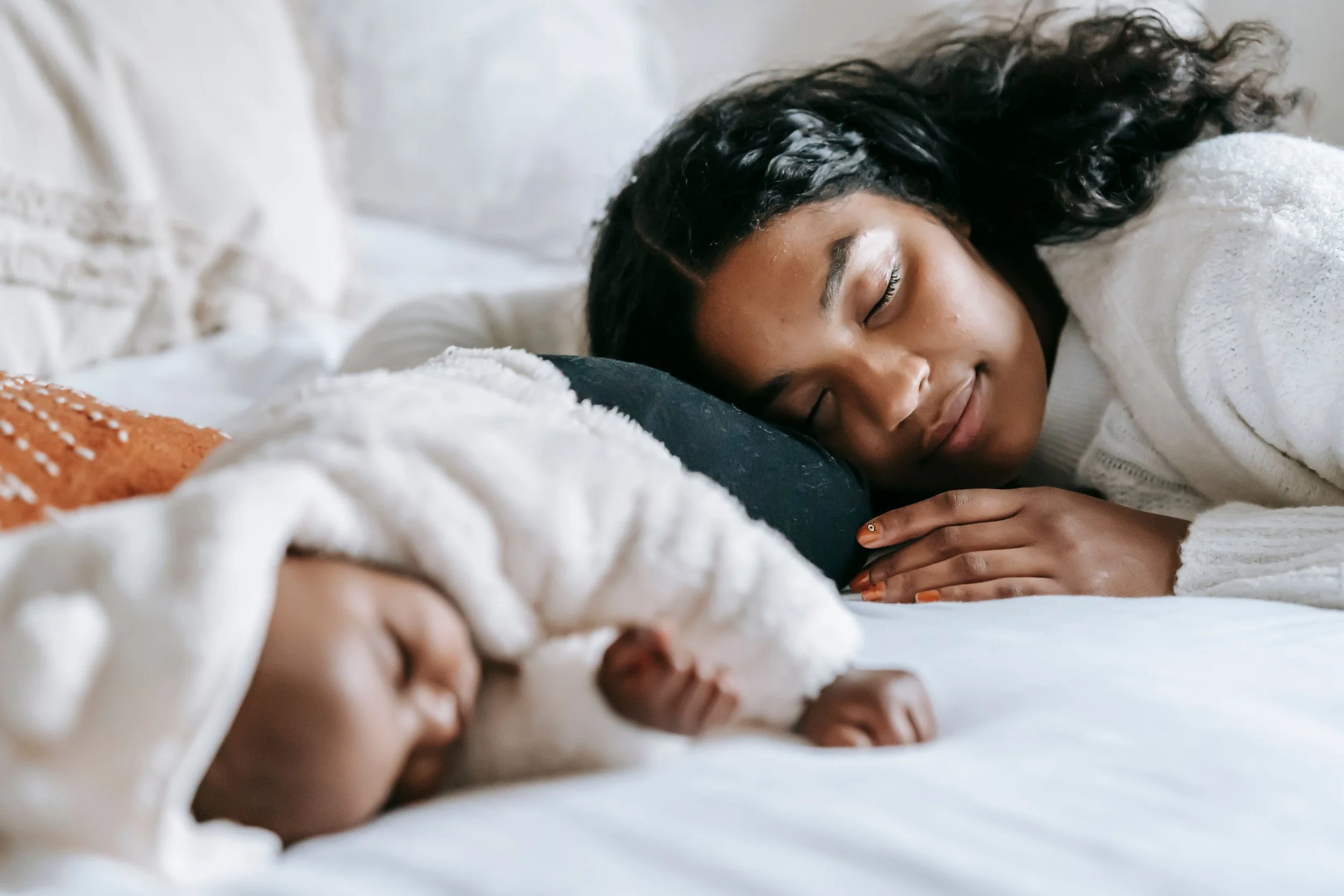 Mother and baby sleeping peacefully in bed, representing postpartum mental health support and rest for new parents.