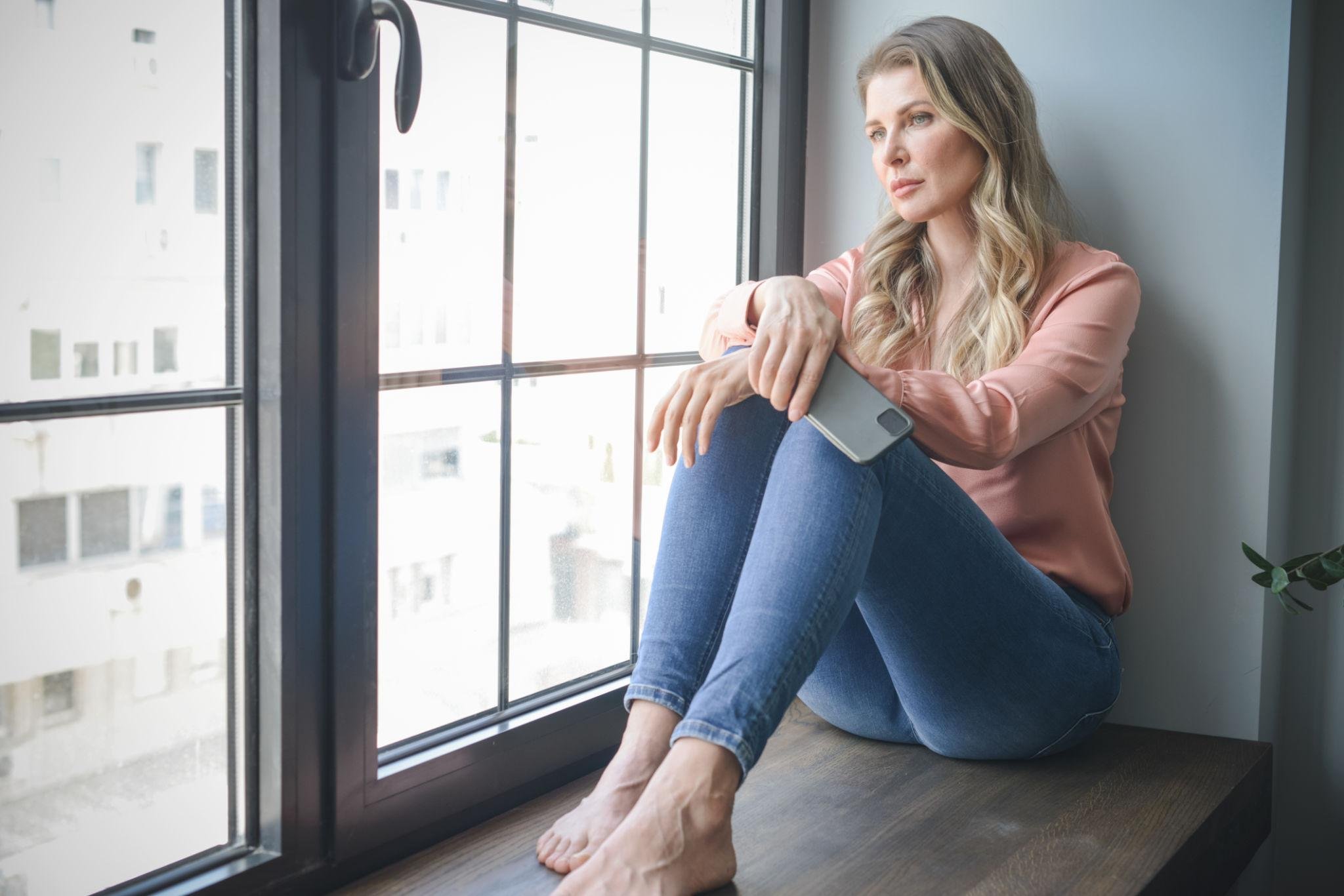 Woman sitting thoughtfully near the window while coping with anxiety and persistent memory doubt