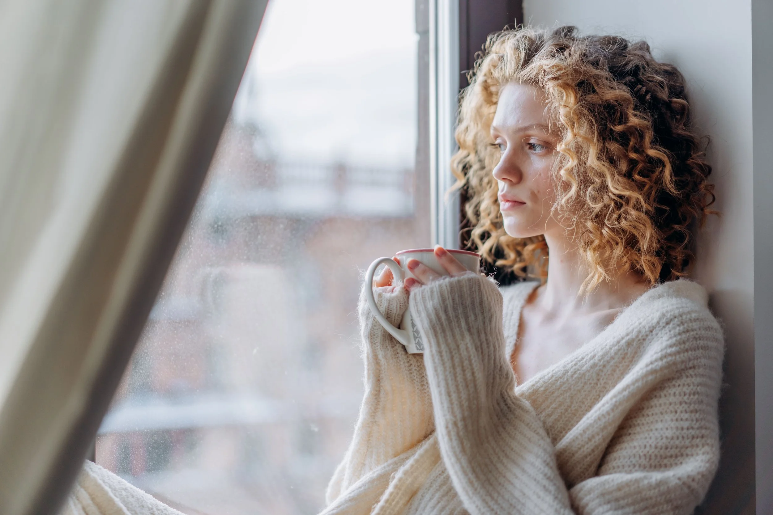 Woman looking thoughtfully out a window while reflecting on OCD recovery and mental health wellness.
