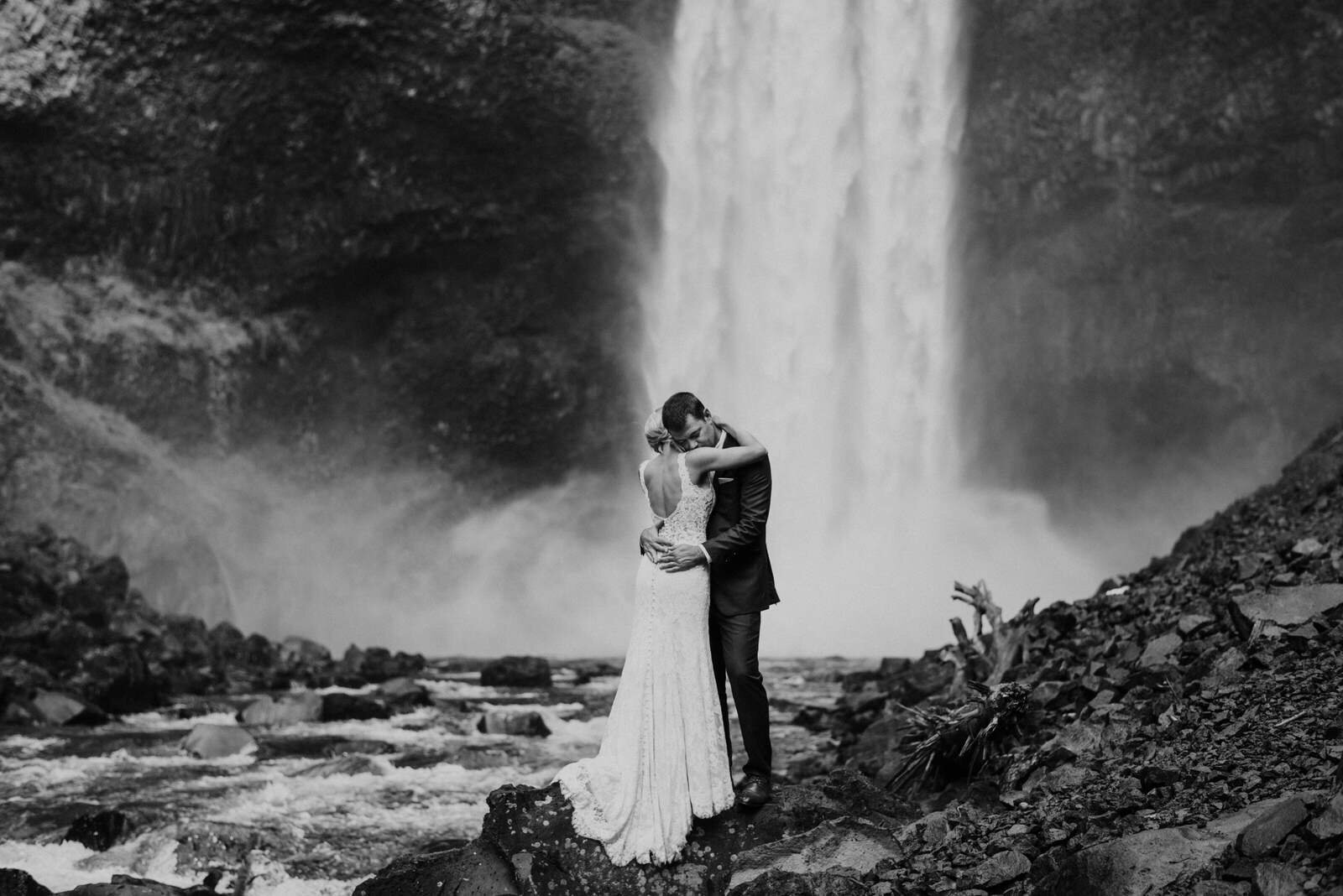 bride and groom hugging under waterfall 