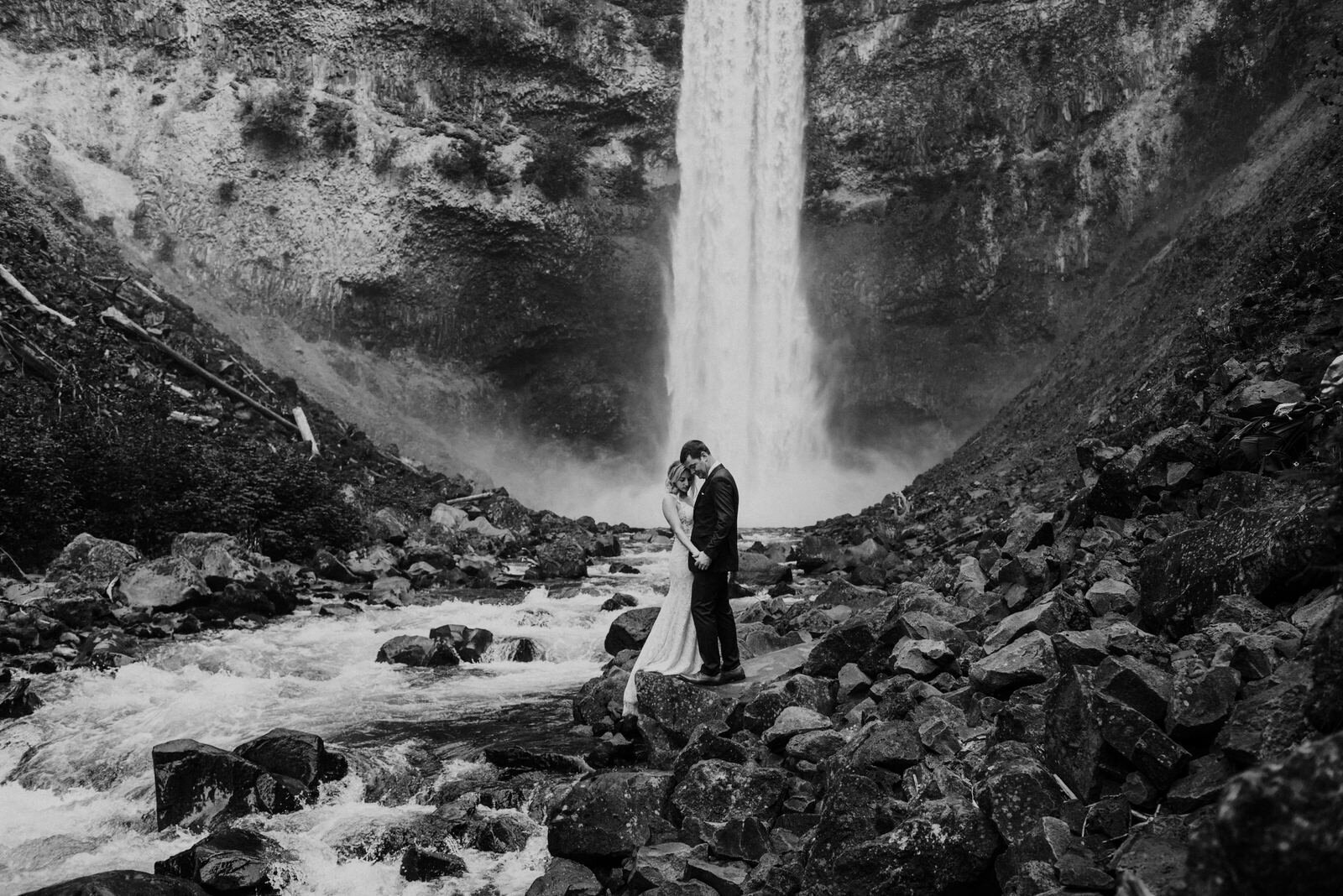 bride and groom holding hands under waterfall