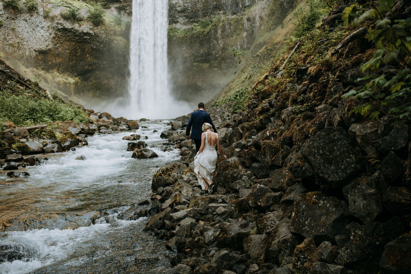 adventurous bride and groom hiking towards waterfall