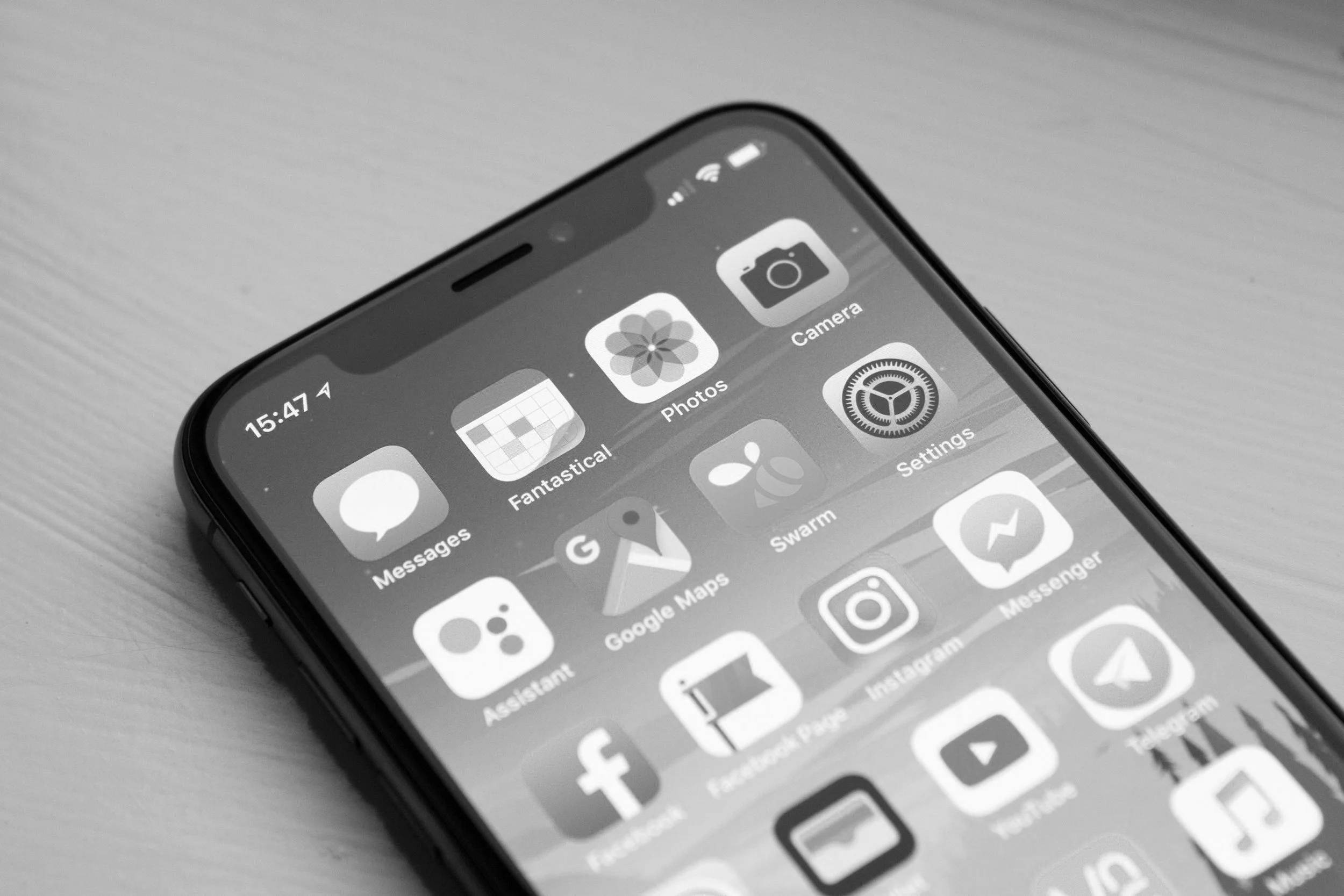 Close-up of a smartphone screen displaying app icons including Messages, Photos, Camera, Google Maps, Instagram, Facebook, YouTube, and Messenger on a wooden surface.