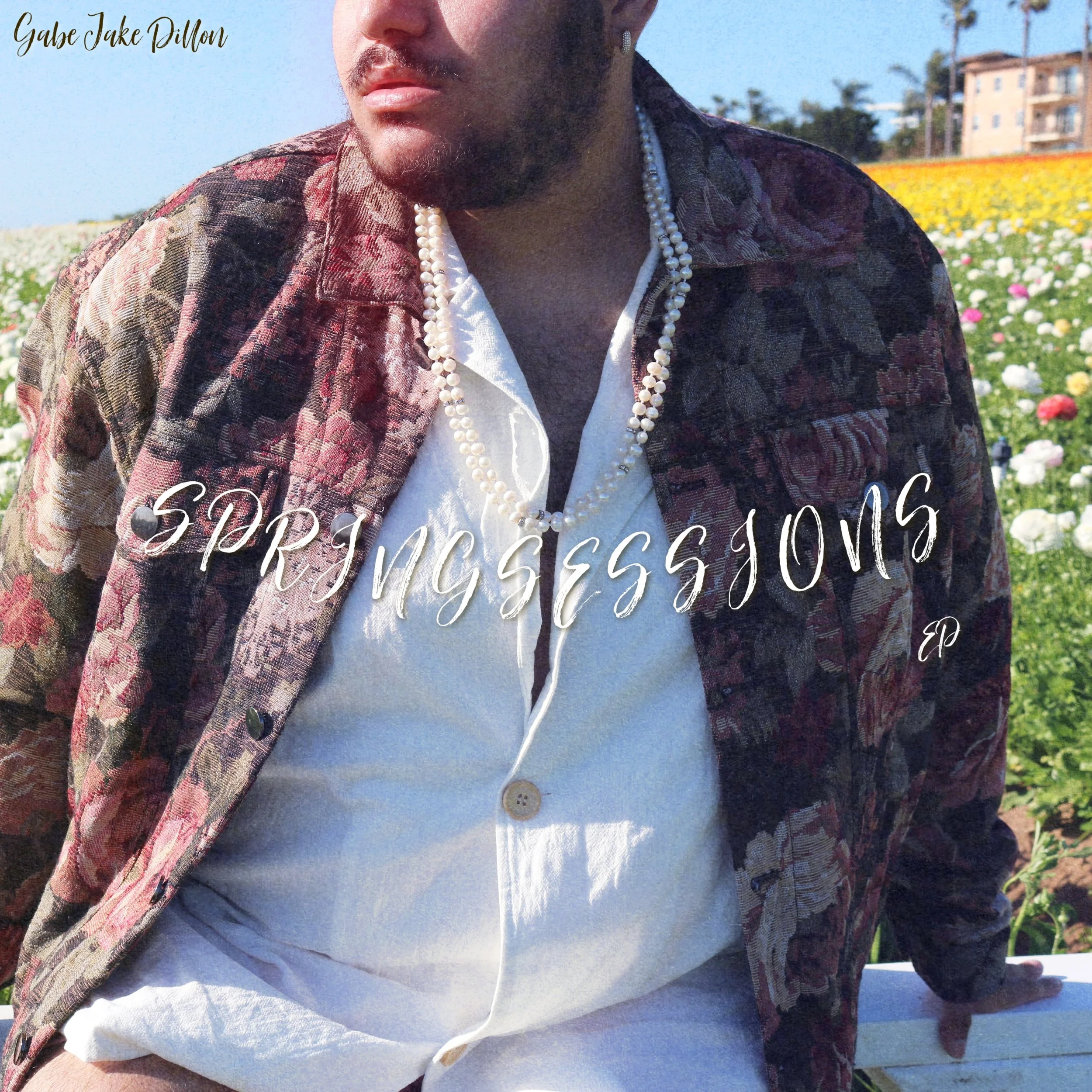 A person with a beard and pearl necklace standing in a field of flowers wearing a patterned jacket and white shirt with text 'SPRINGESSIONS EP' overlaid.