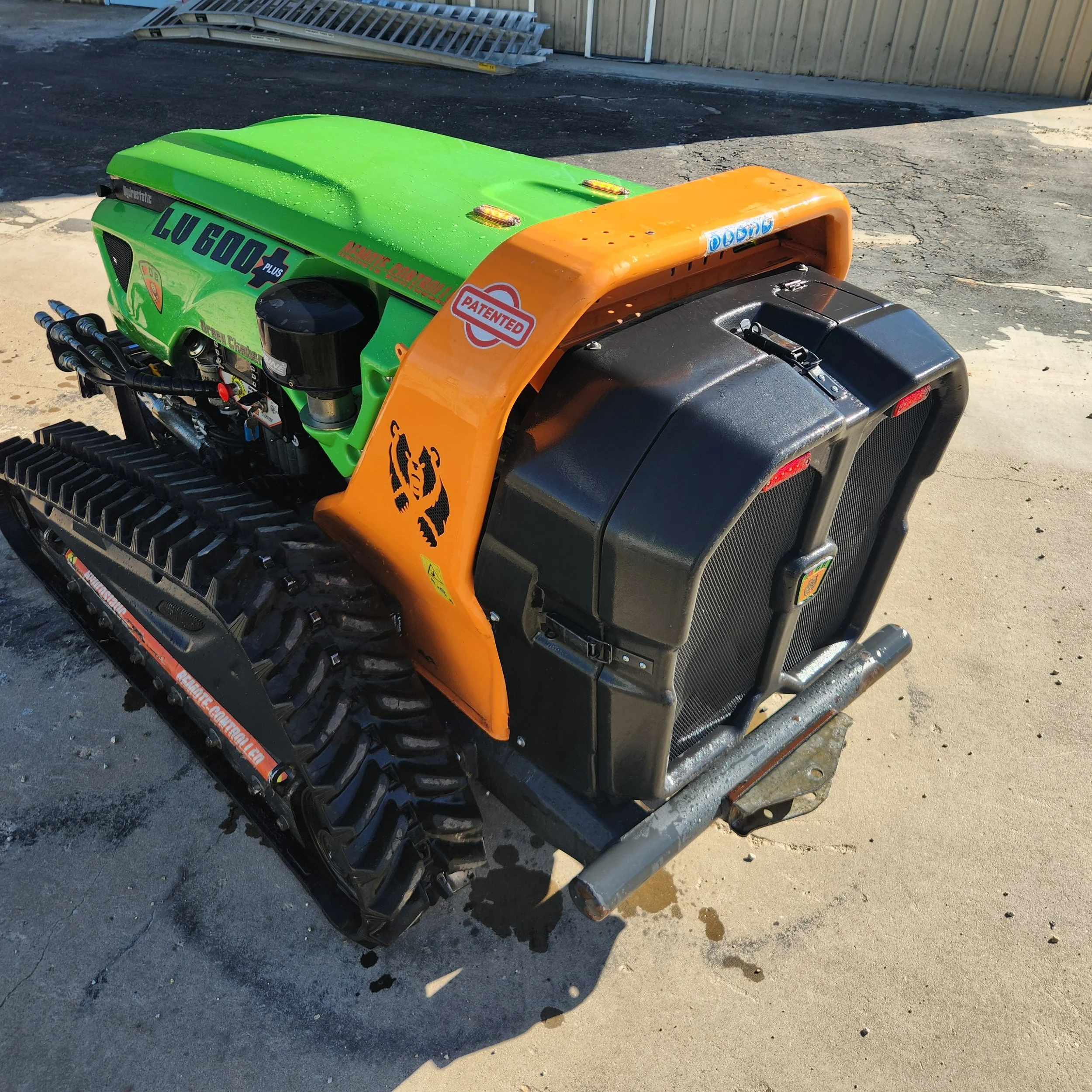 A small tracked vehicle with a green and orange body, black radiator, and a lion logo on the side. It appears to be a modified or custom machine, possibly for industrial or recreational use.