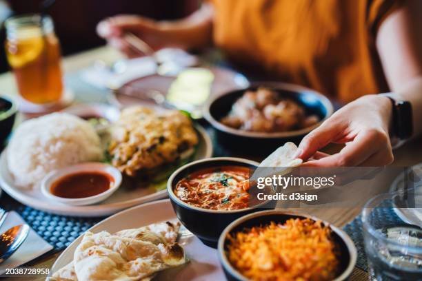 A table with various Indian dishes, including naan bread, rice, curry, and a side of sauce, with drinks and people around dining.