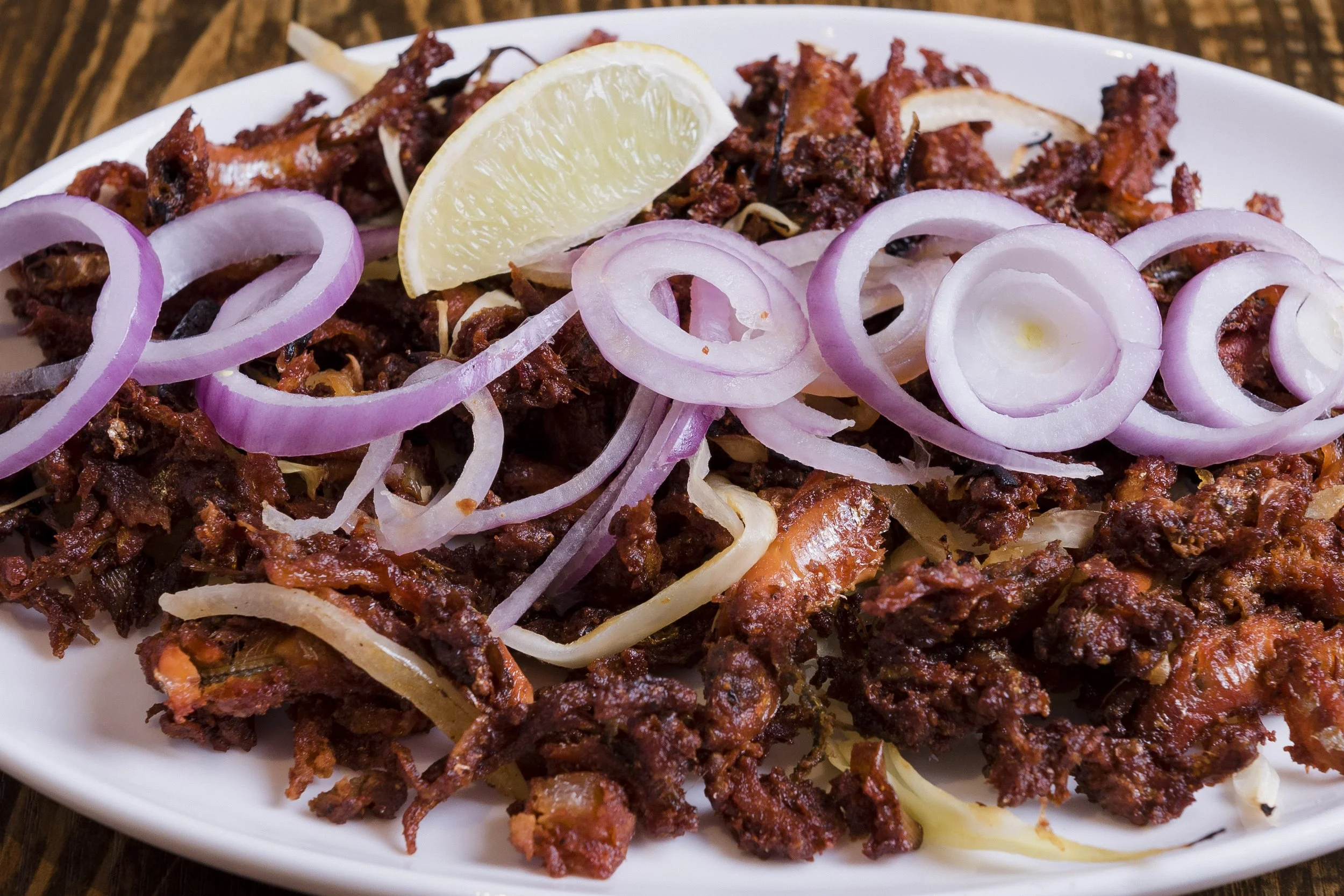Plate of spicy shredded beef garnished with sliced onions and a lemon wedge.